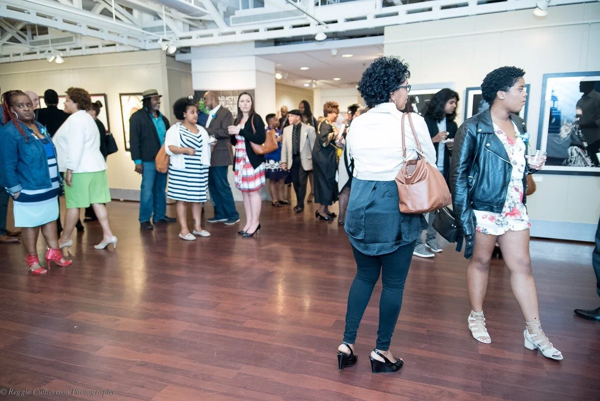 People viewing artwork in an art gallery with wood flooring and white walls.
