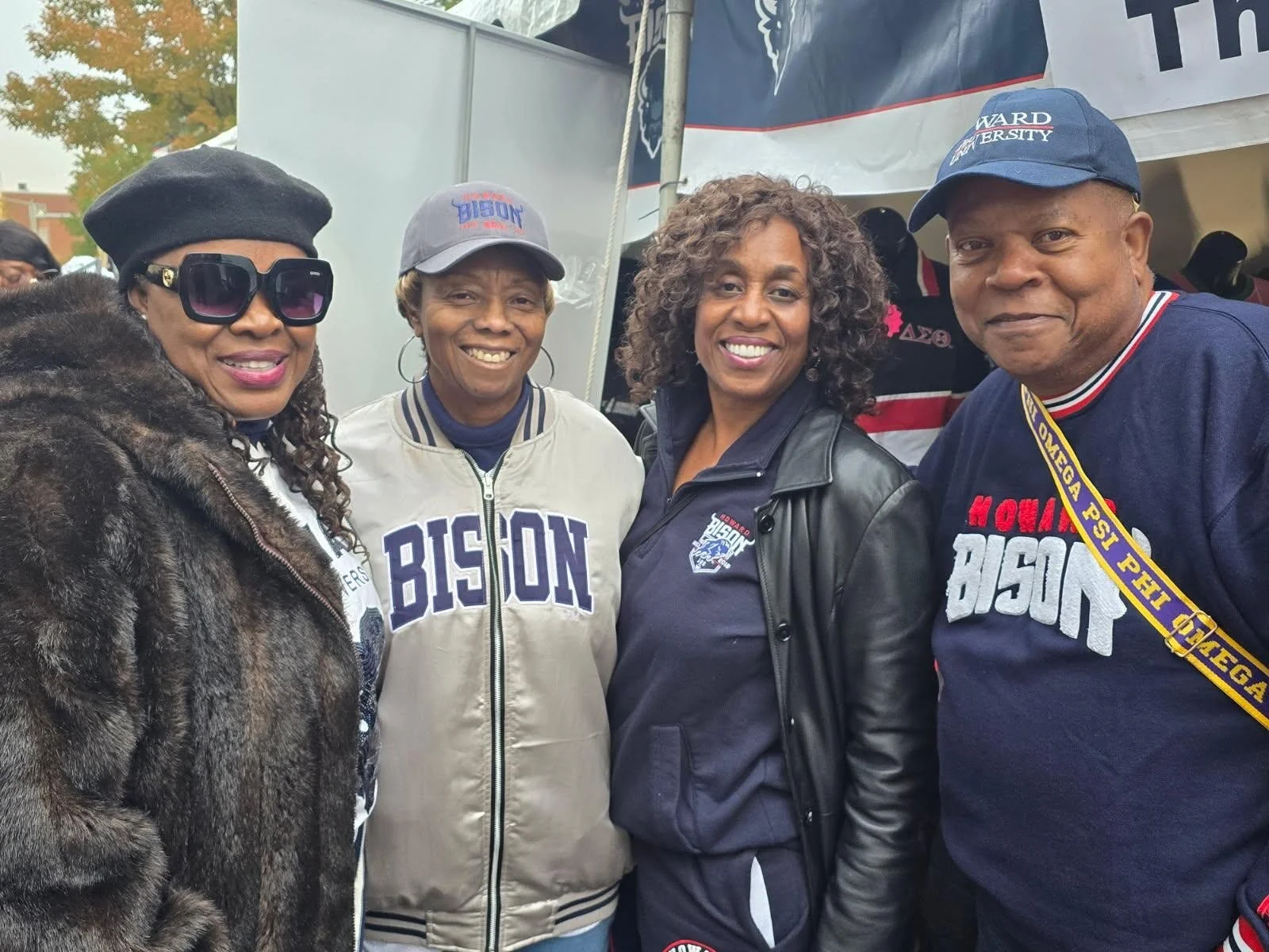 Four people standing together outdoors, smiling. They are wearing clothing and hats supporting Bison, indicating they are at a Bison-themed event or gathering.