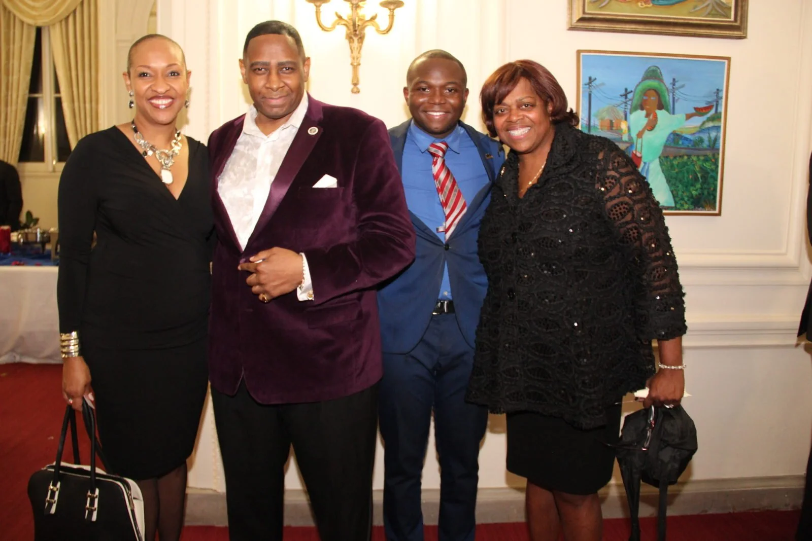 Four people dressed in formal attire standing together indoors at a social event, smiling at the camera.