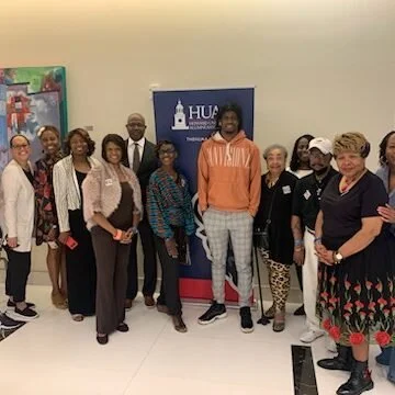 Group of people standing together for a photo indoors, with a banner in the background that says 'HUB' and an artwork on the wall.