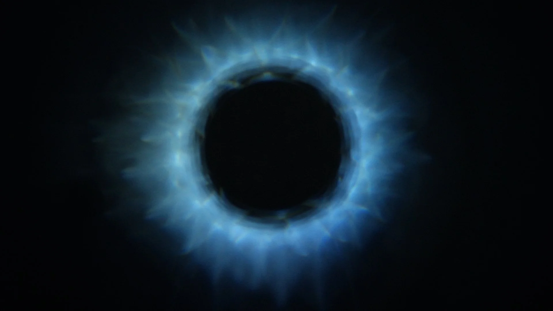 Close-up of a circular optical illusion with glowing blue light and radiating starburst effects in a dark background.