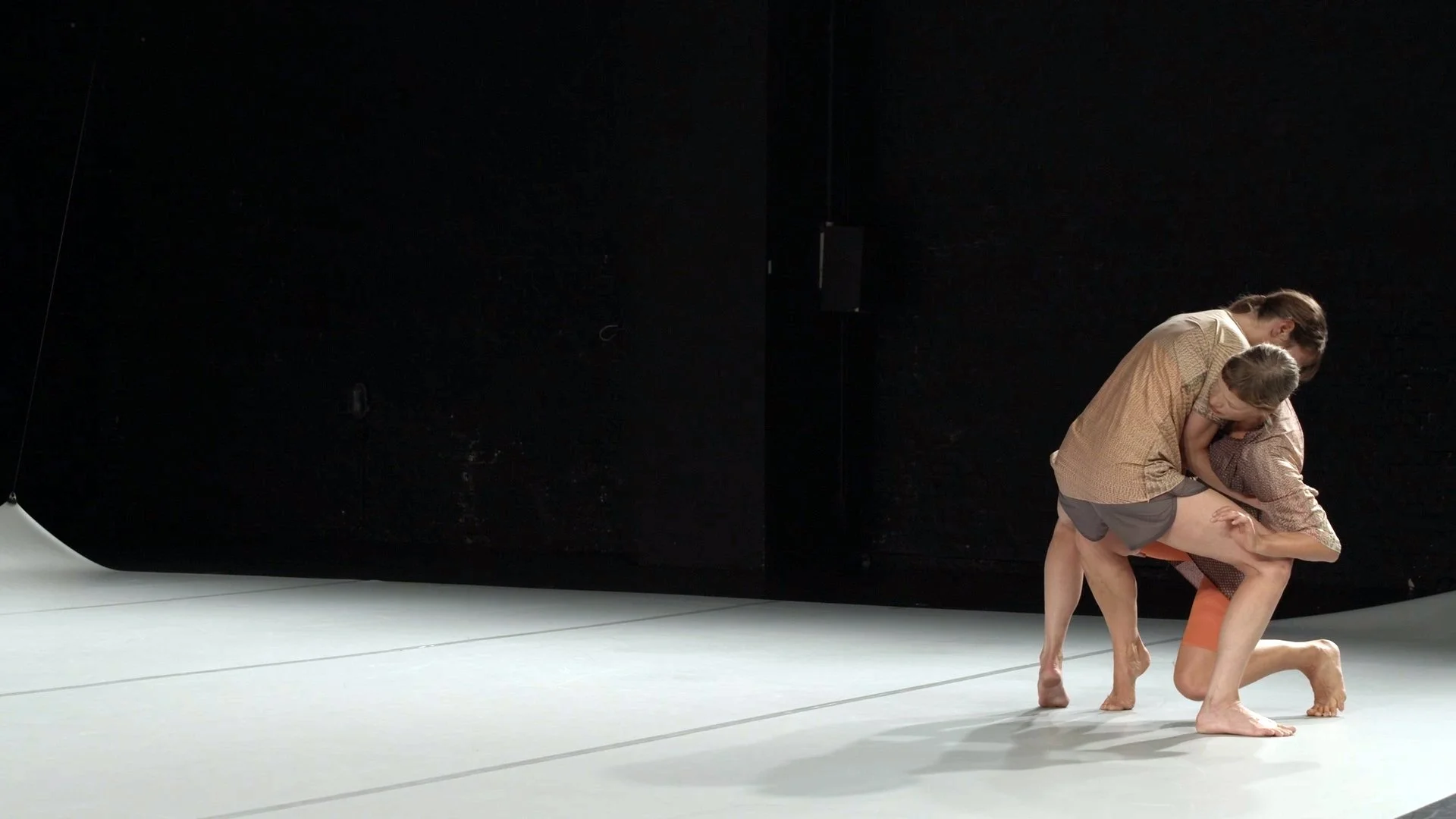 Two dancers perform a contemporary dance routine on stage, with a black backdrop and minimal lighting.