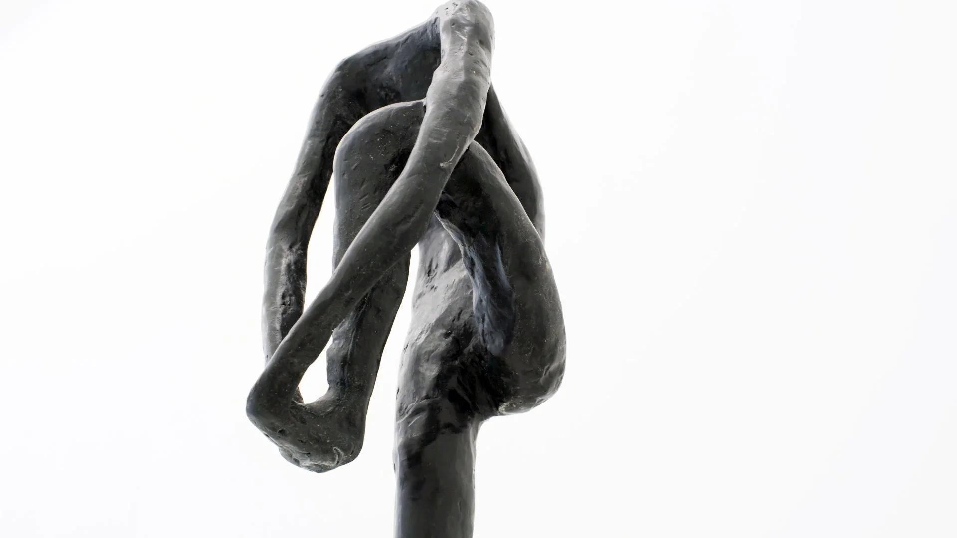 Close-up of a dark metal sculpture of a hand holding a piece of cloth or a similar object against a plain white background.