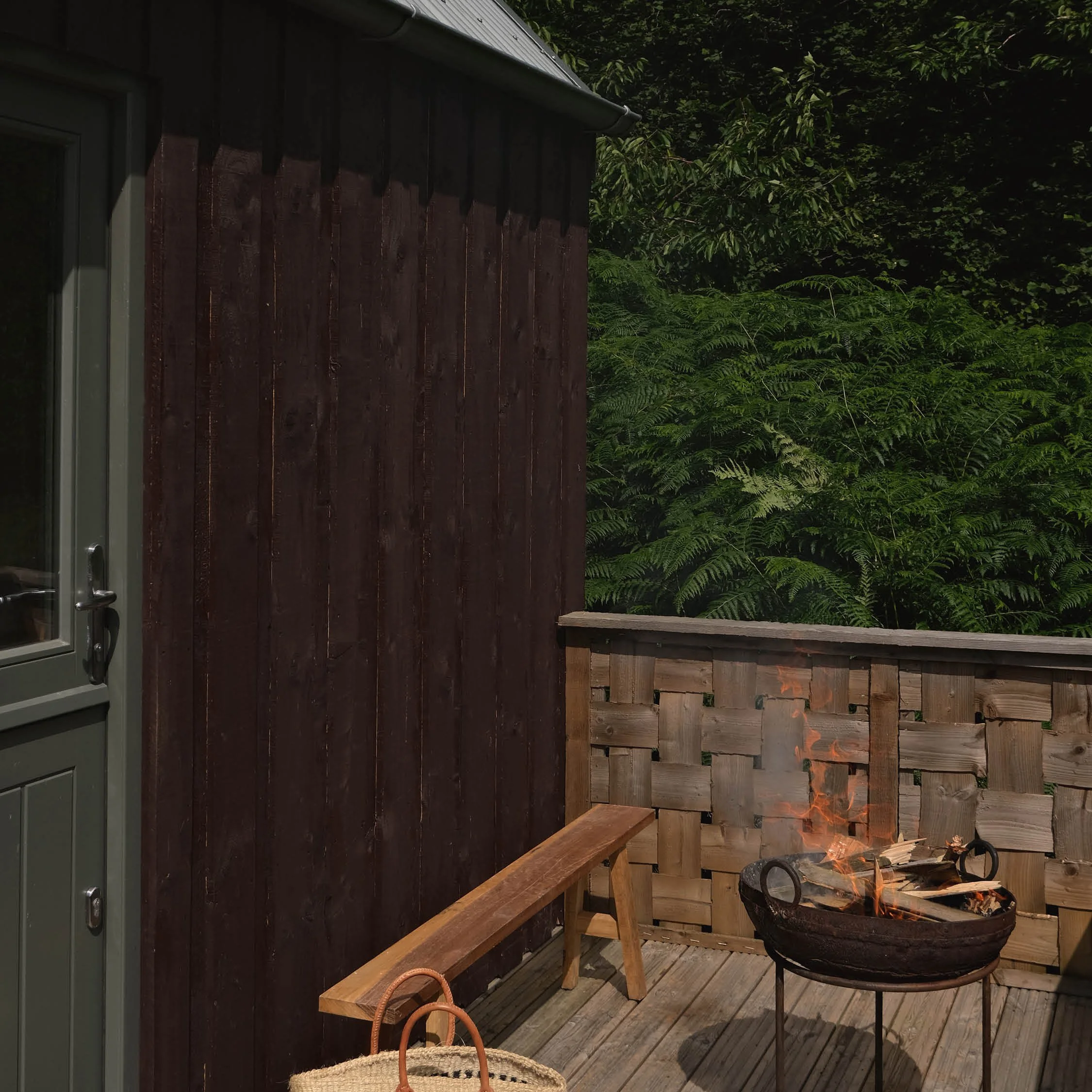 A cozy outdoor deck with a fire pit, wooden bench, and surrounding greenery.