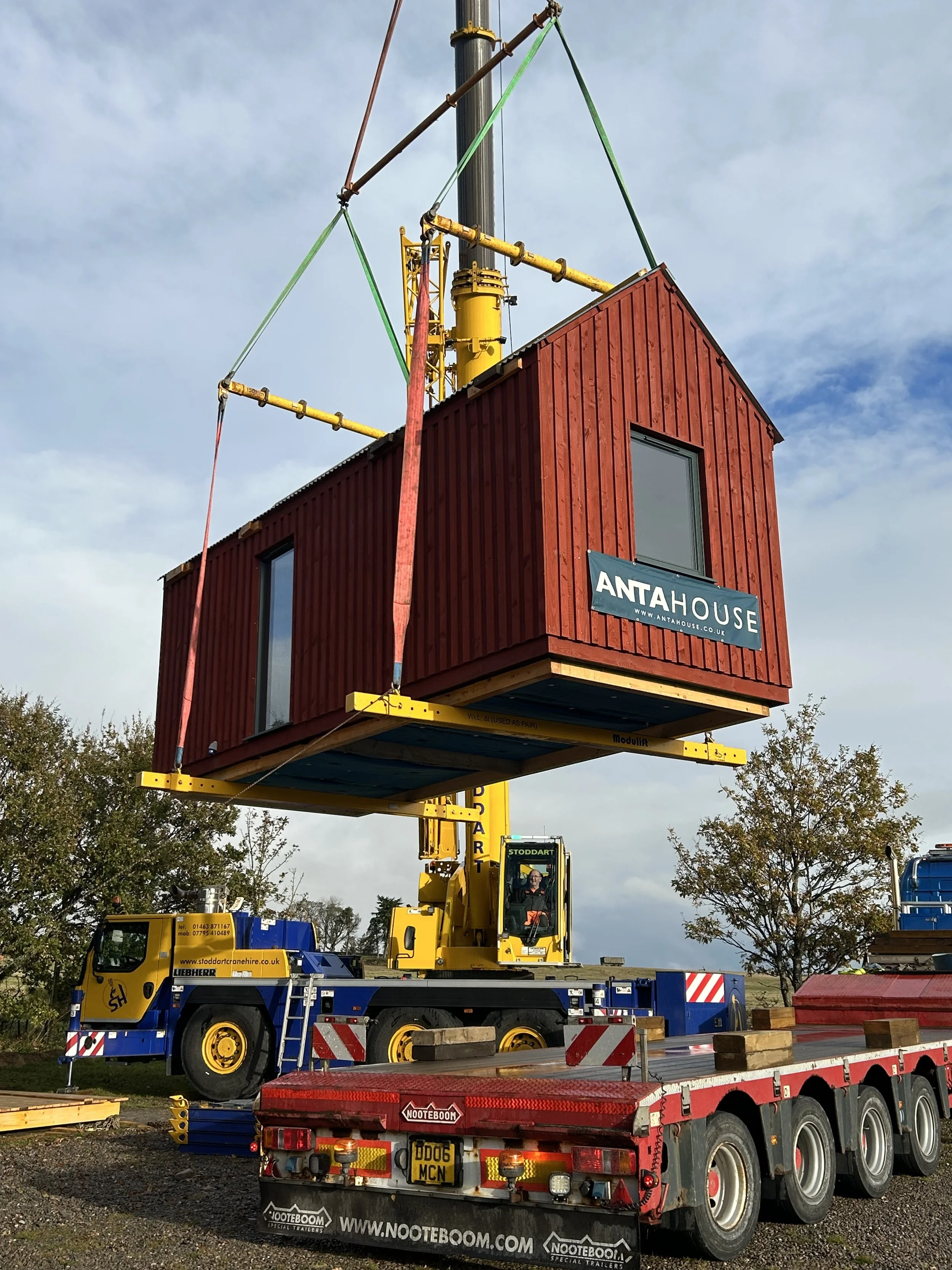 A crane lifting a red hut onto a flatbed trailer.