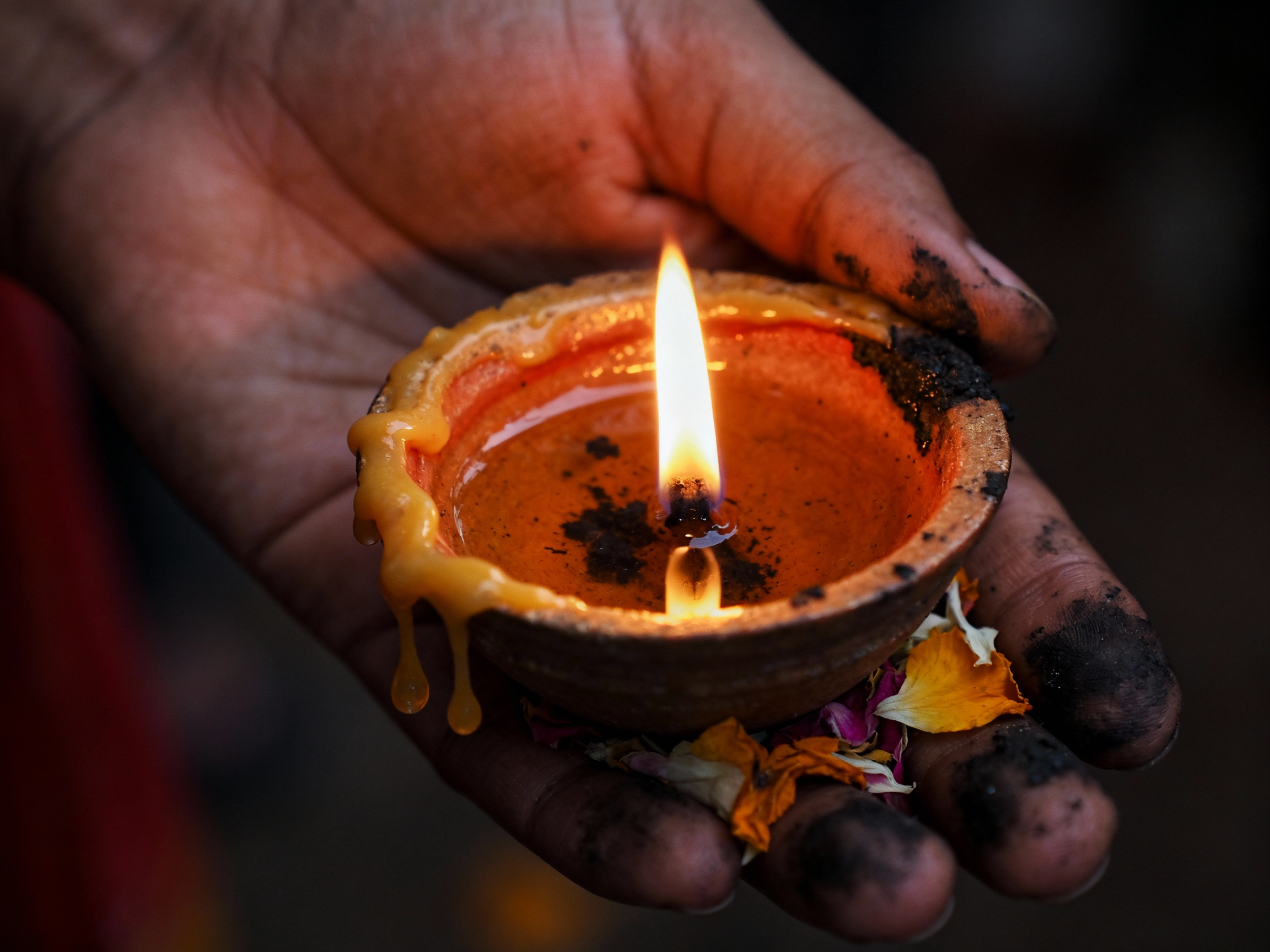 Main d'une personne indienne spirituelle tenant une petite bougie allumée dans un bol en terre cuite, entourée de fleurs colorées.