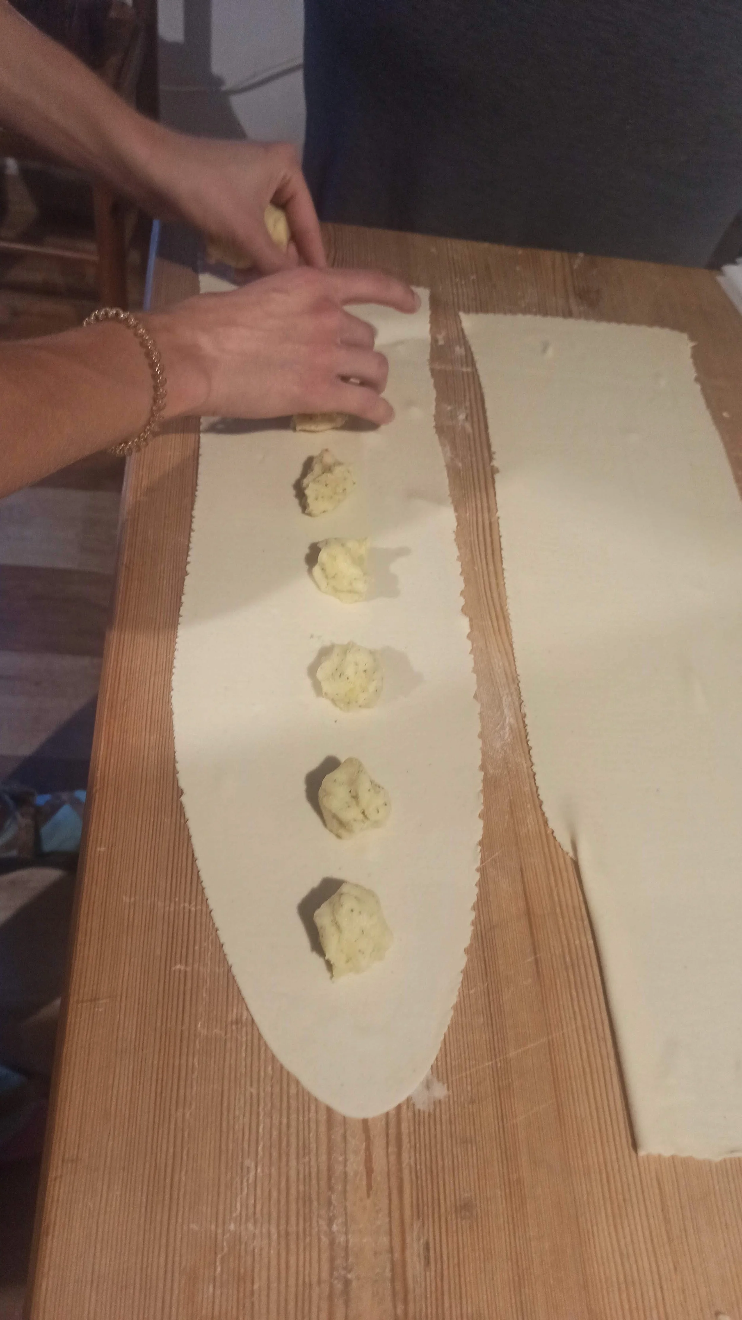 Hands placing dollops of a filling onto a sheet of pastry dough on a wooden table.