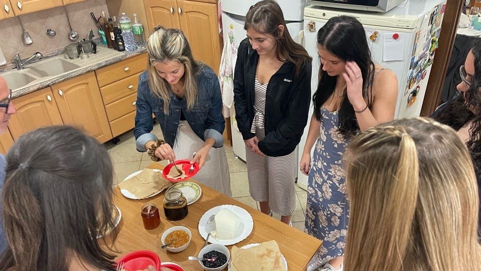 A group of women gathered around a kitchen table, making or preparing food with various ingredients and utensils.