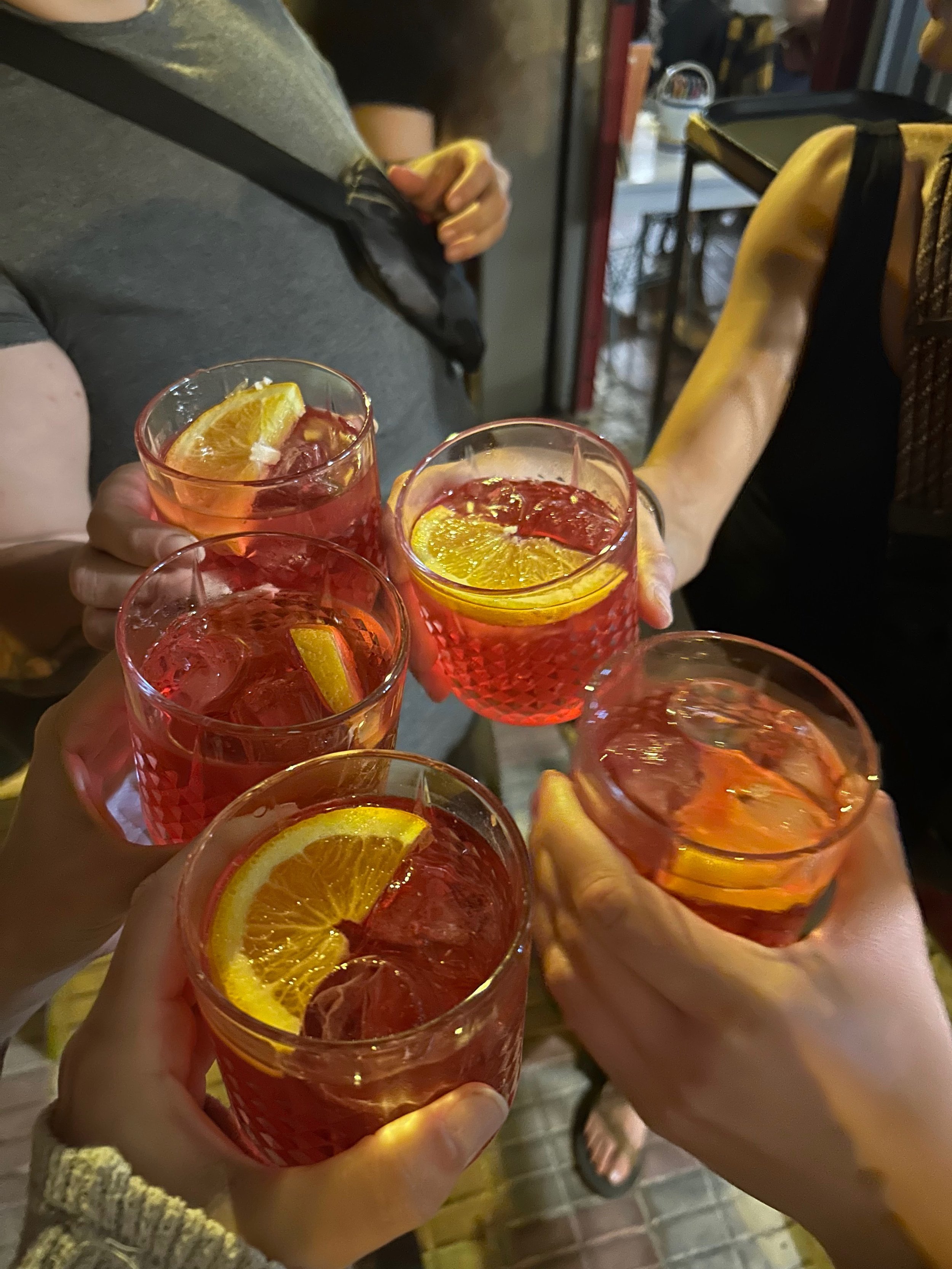 Group of friends clinking glasses of red cocktail drinks garnished with lemon slices at a social gathering.