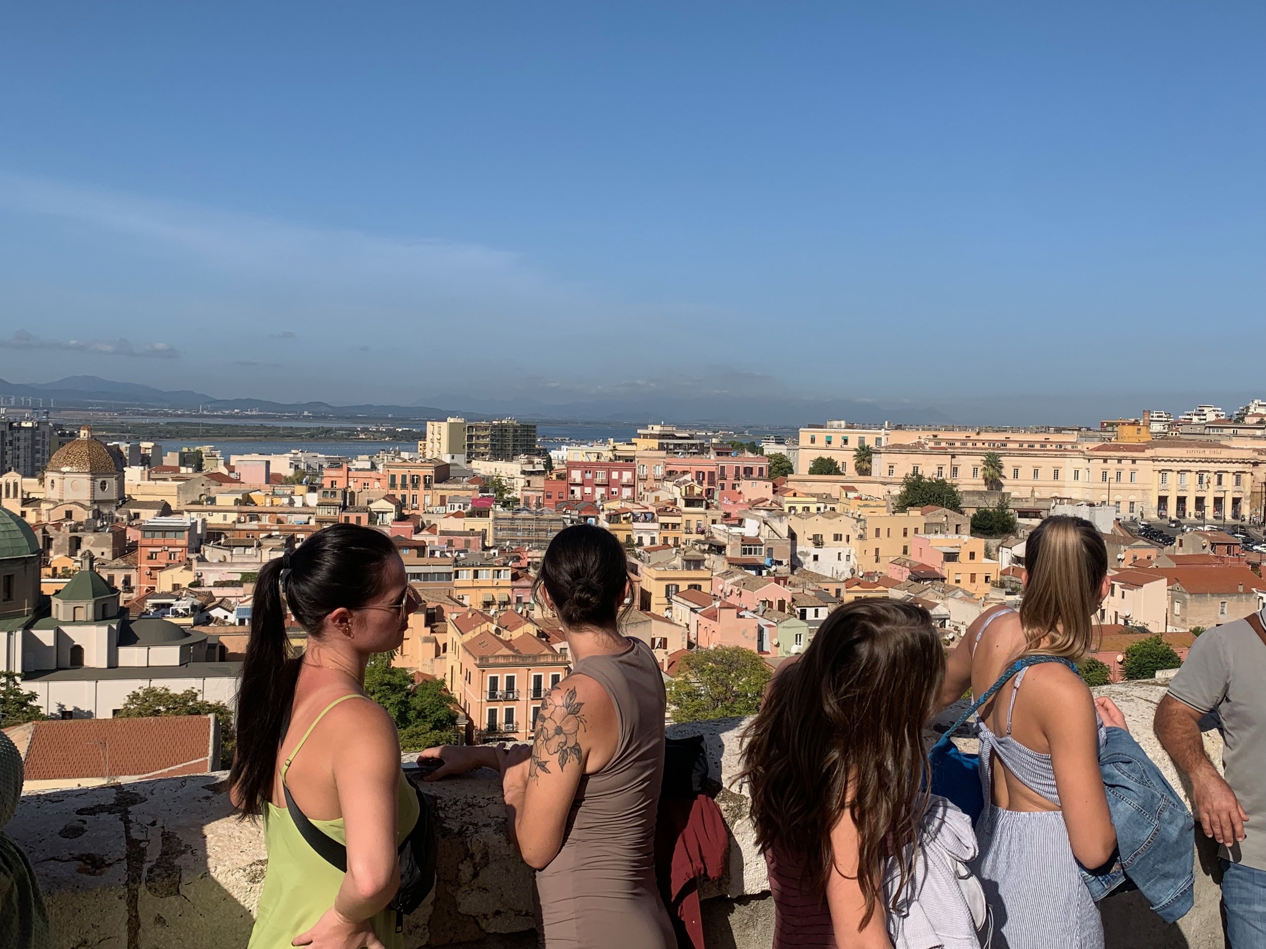 View of a cityscape with colorful buildings under a clear blue sky, with several women standing and looking at the view in the foreground.