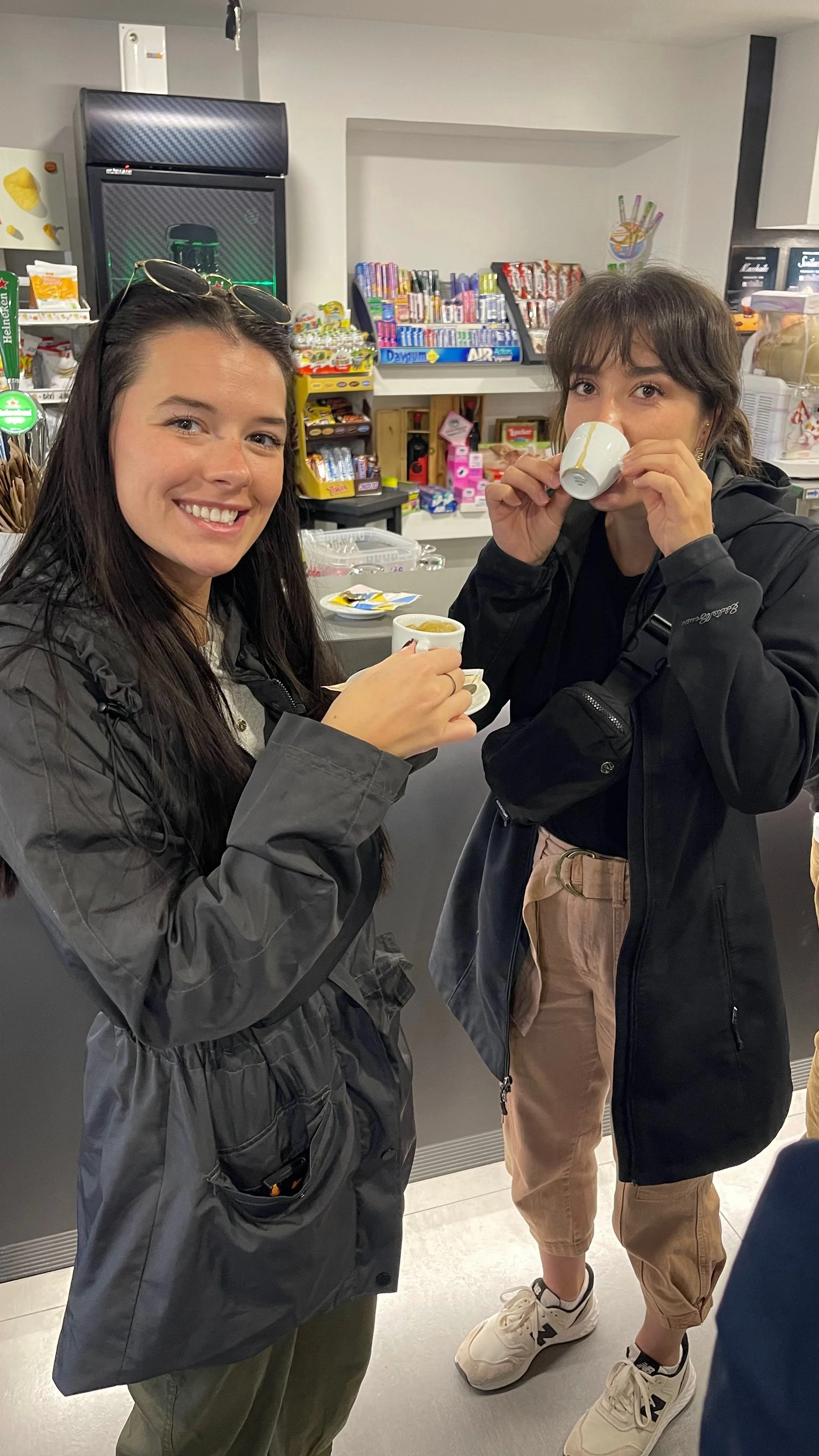 Two women enjoying coffee in a cafe, holding cups and smiling at the camera.