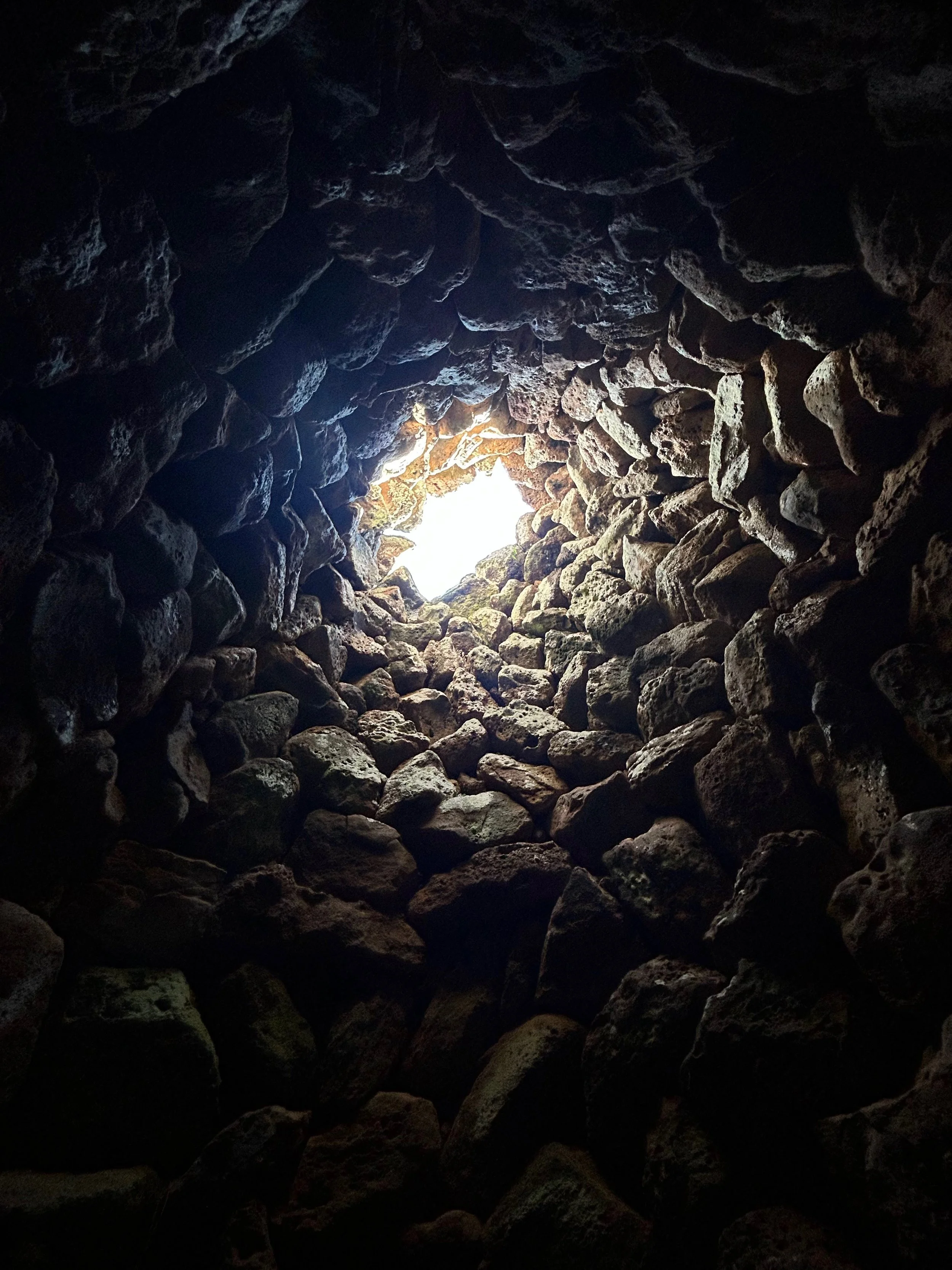 Looking up through a stone well with rough, irregular stones and light at the top.