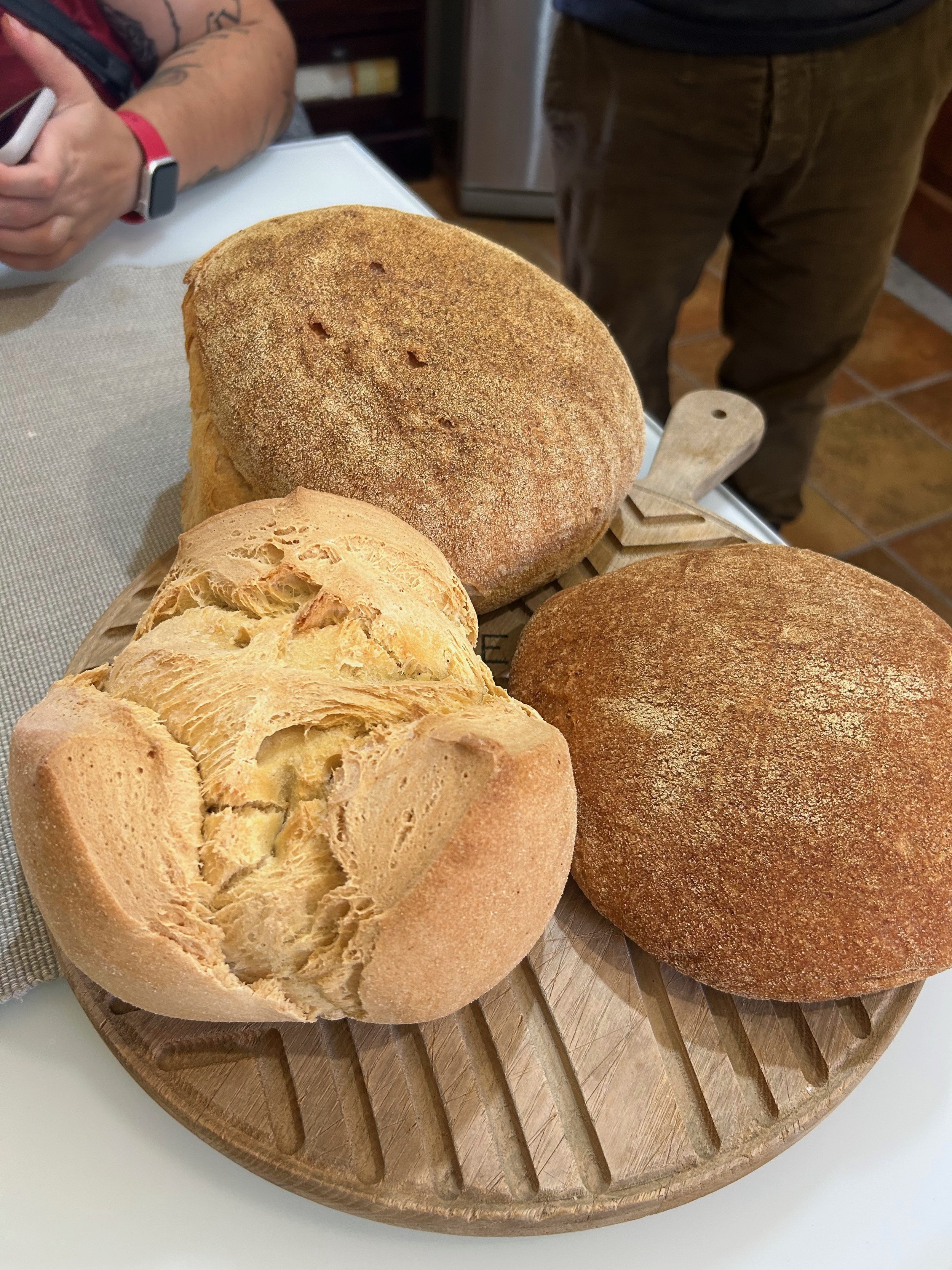 Three types of bread on a wooden cutting board, with one bread torn open showing its interior.