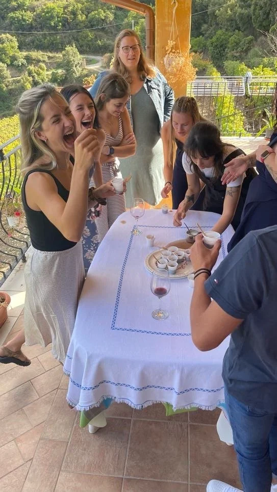Group of women and girls gathered around a table outdoors, enjoying a social gathering with drinks and desserts.