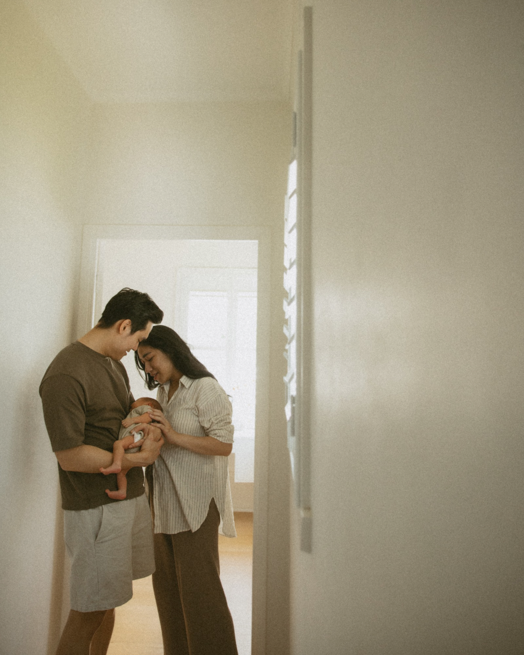 A couple holding a newborn baby in a hallway, looking at the baby lovingly.