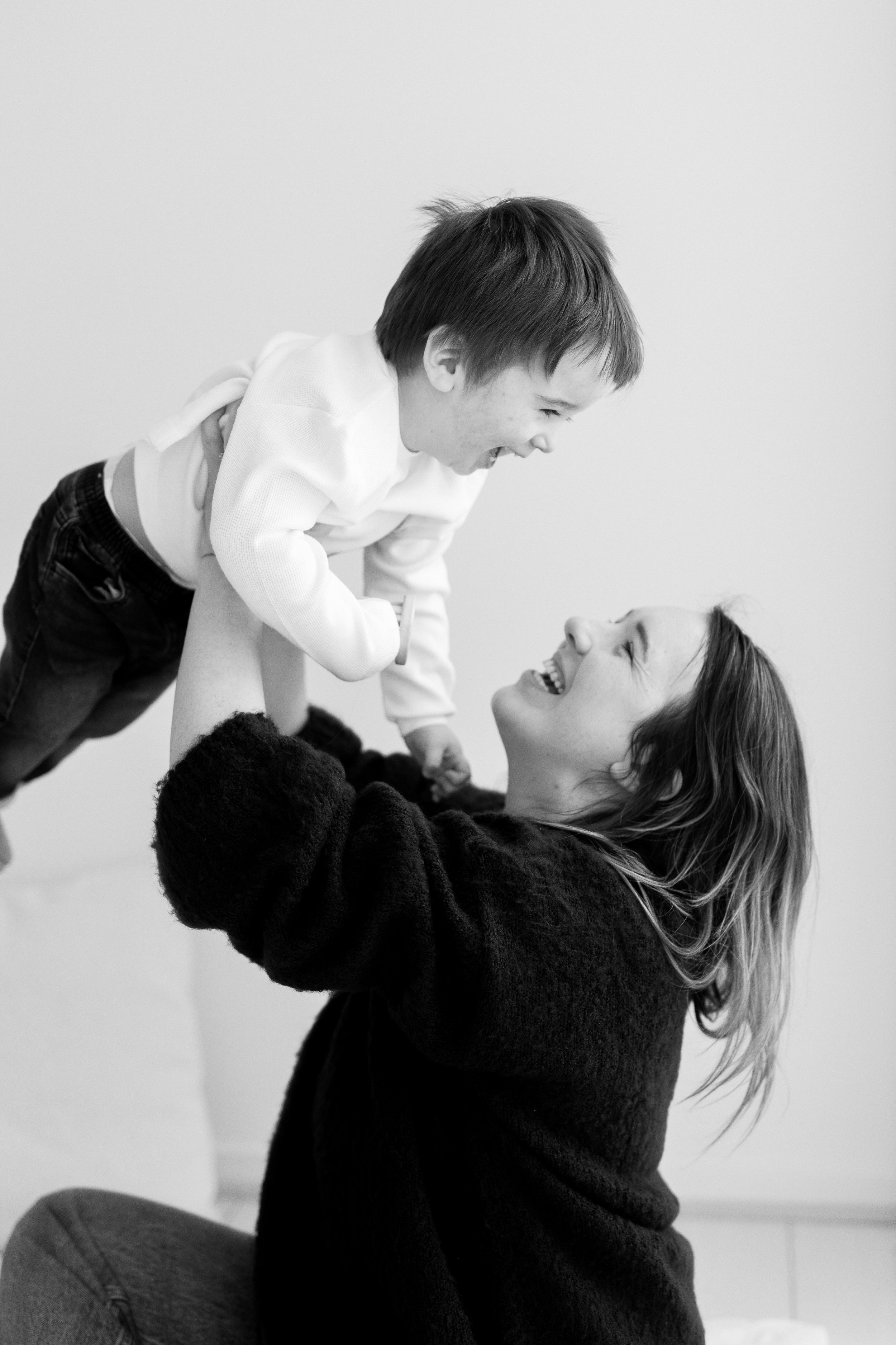 A woman lifting a young boy playfully while both are smiling.