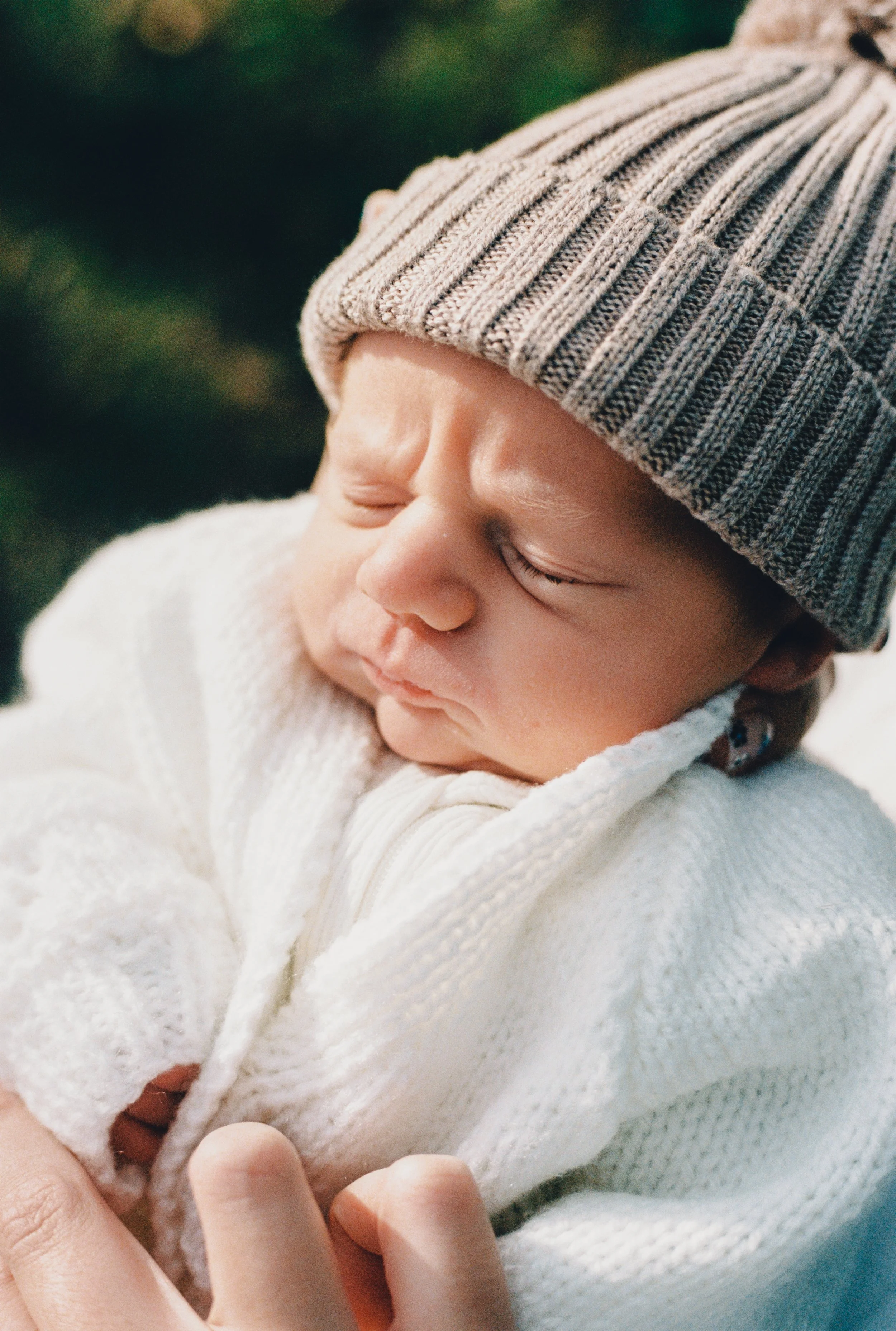 Close-up of a sleeping newborn baby wearing a gray striped knit hat and a white knit sweater.