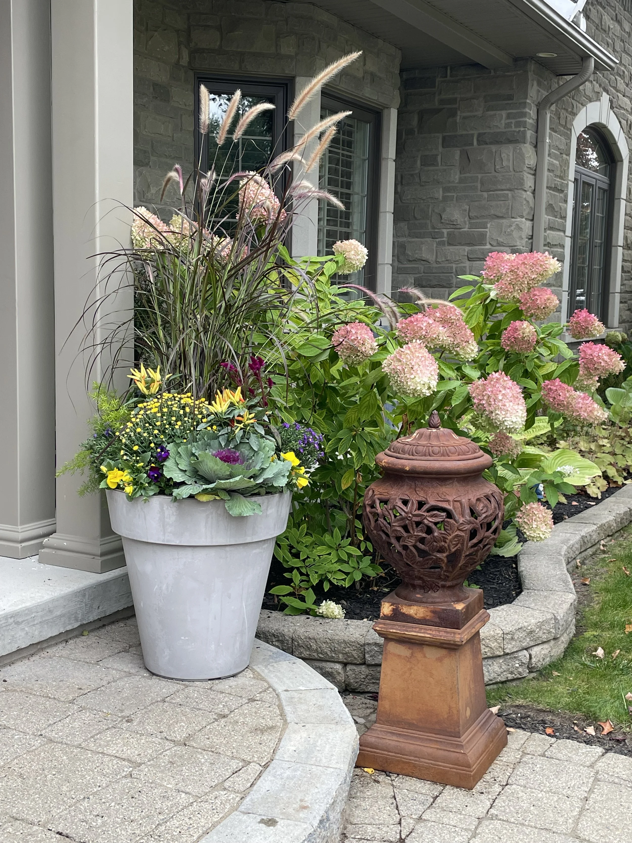 A stunning fall planter filled with colourful harvest inspired flowers and tall ornamental grass, created by Fleuristic.