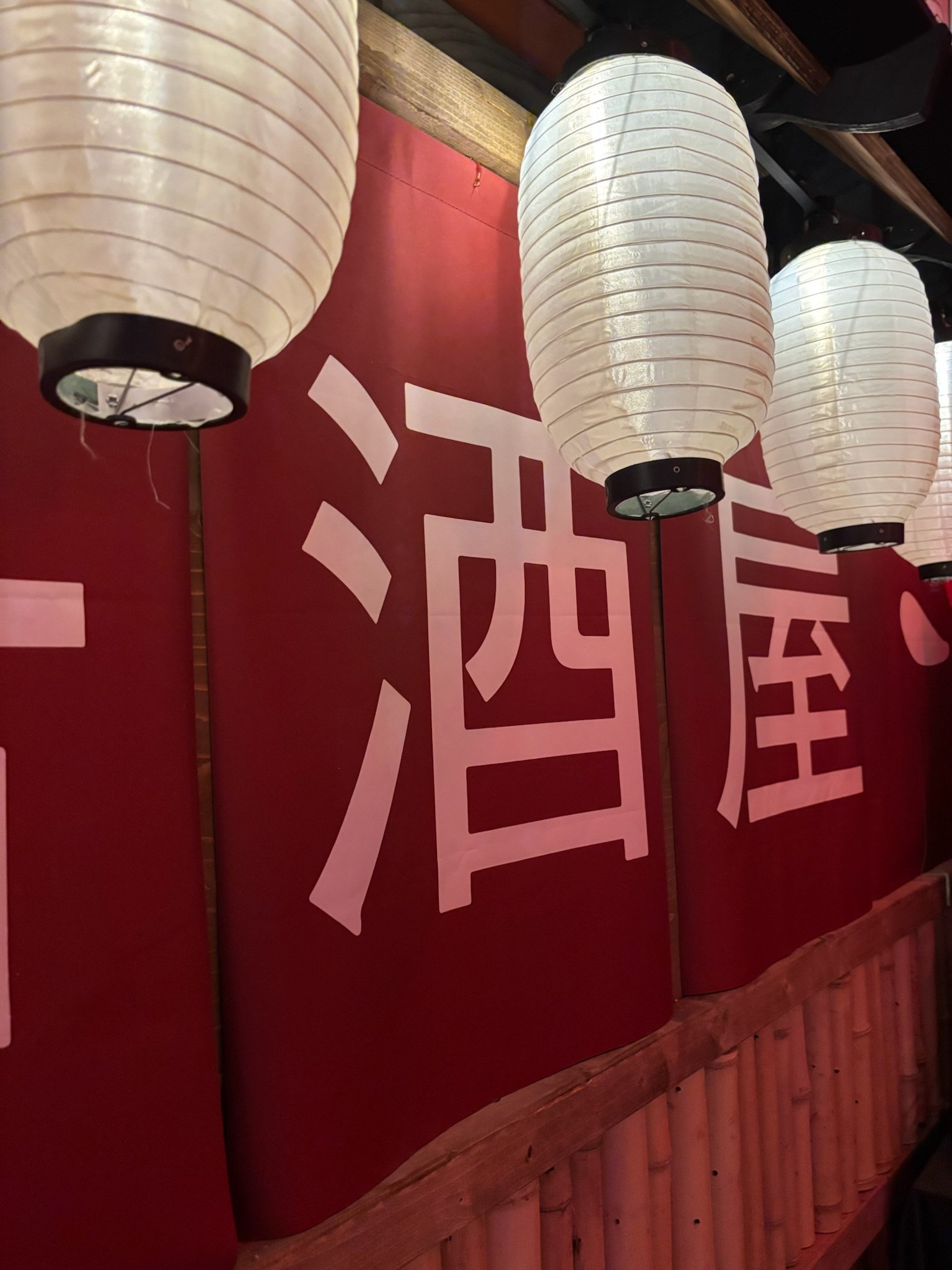Japanese paper lanterns hanging above large red panels with white Japanese characters.