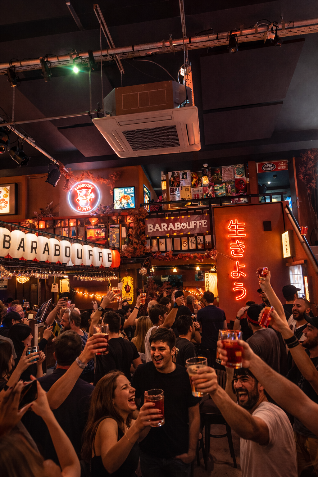 People celebrating and raising drinks in a lively bar or restaurant with neon signs and Japanese-themed decor.