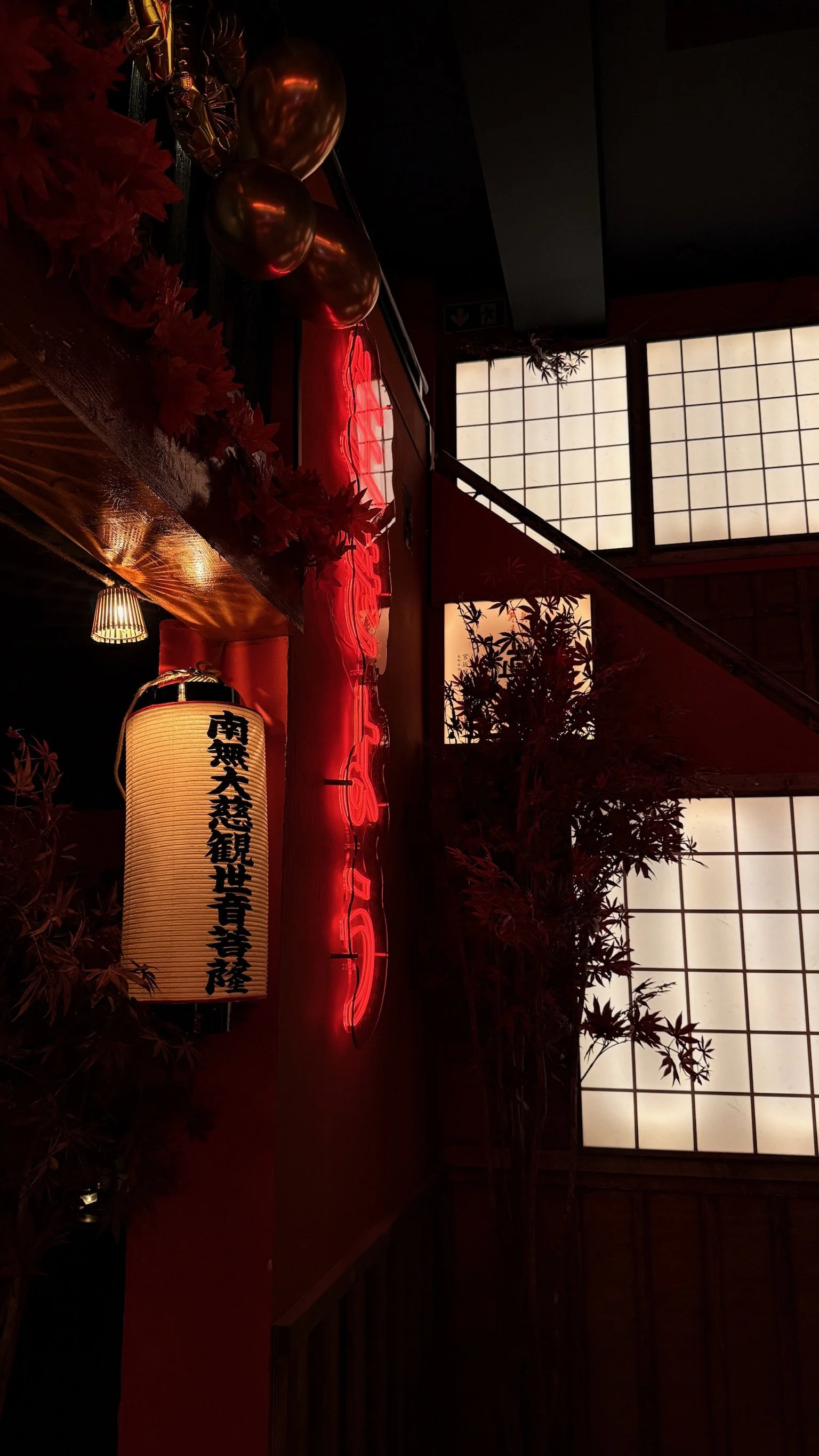 Interior of a Japanese-style room with shoji screen windows, red neon sign, paper lantern with Japanese writing, and decorative red leaves and balloons.
