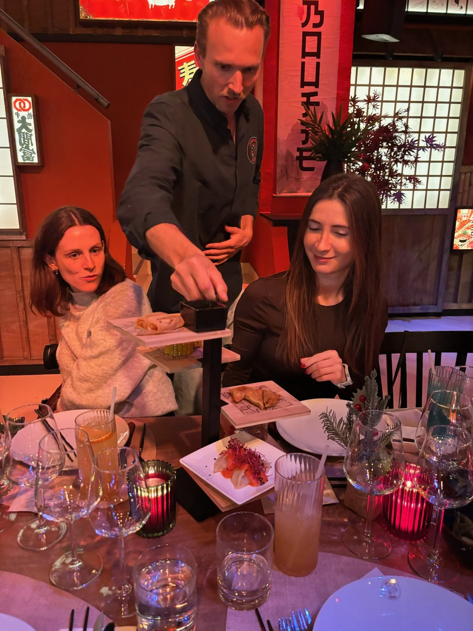 A waiter serving food to two women at a table in a restaurant with Asian decor.
