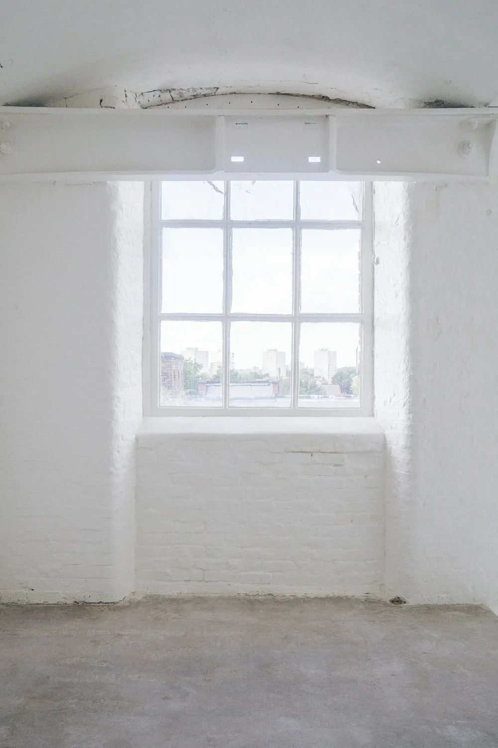 Empty white room with a large window showing cityscape view outside.