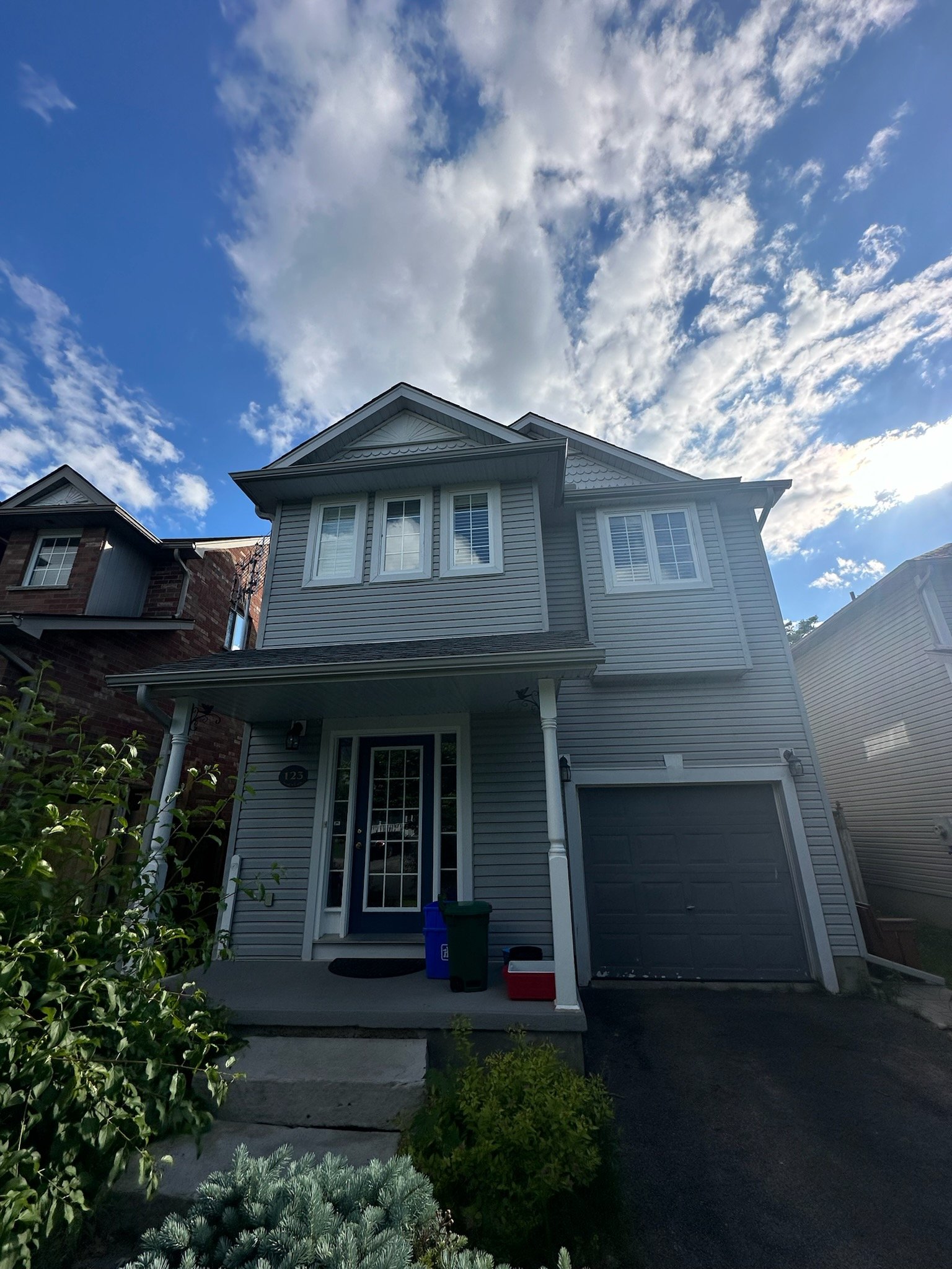 Front view of a two-story suburban house with gray siding and a black garage door, under a partly cloudy sky.