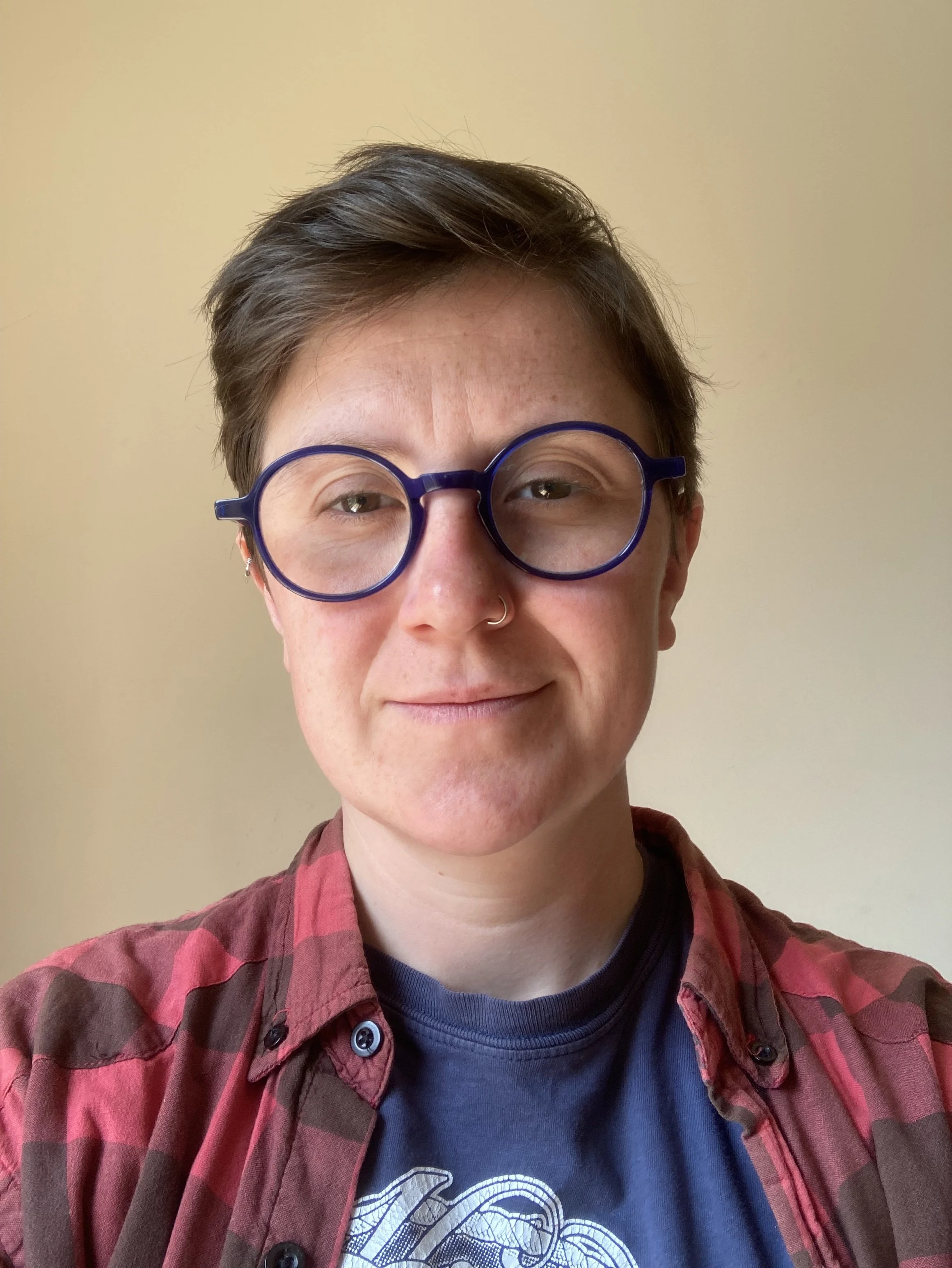 A picture of a woman with short, dark hair, round blue-framed glasses and a red checked shirt.
