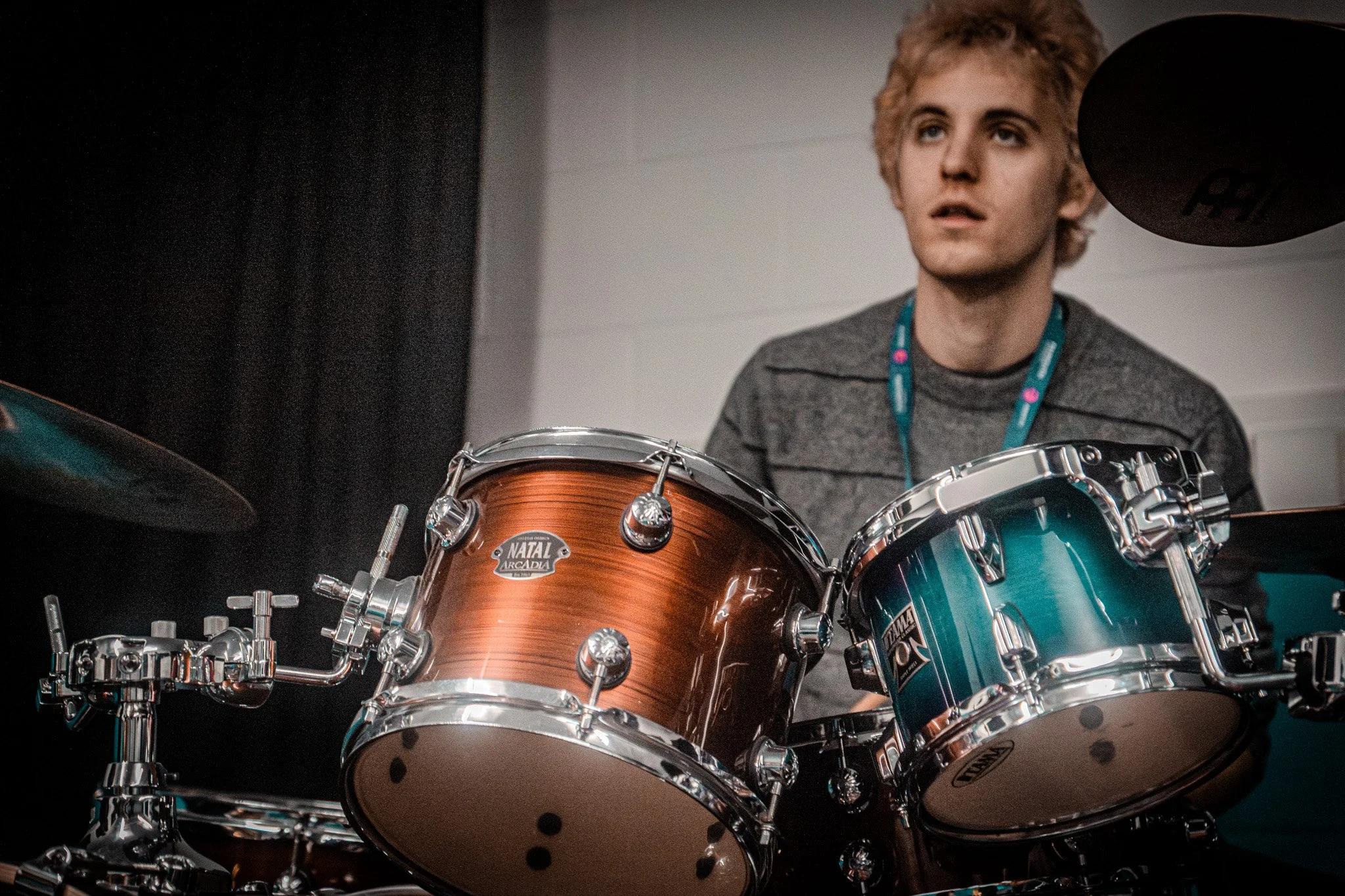 Young man sitting behind a blue and brown drum set in a room with black and white walls.