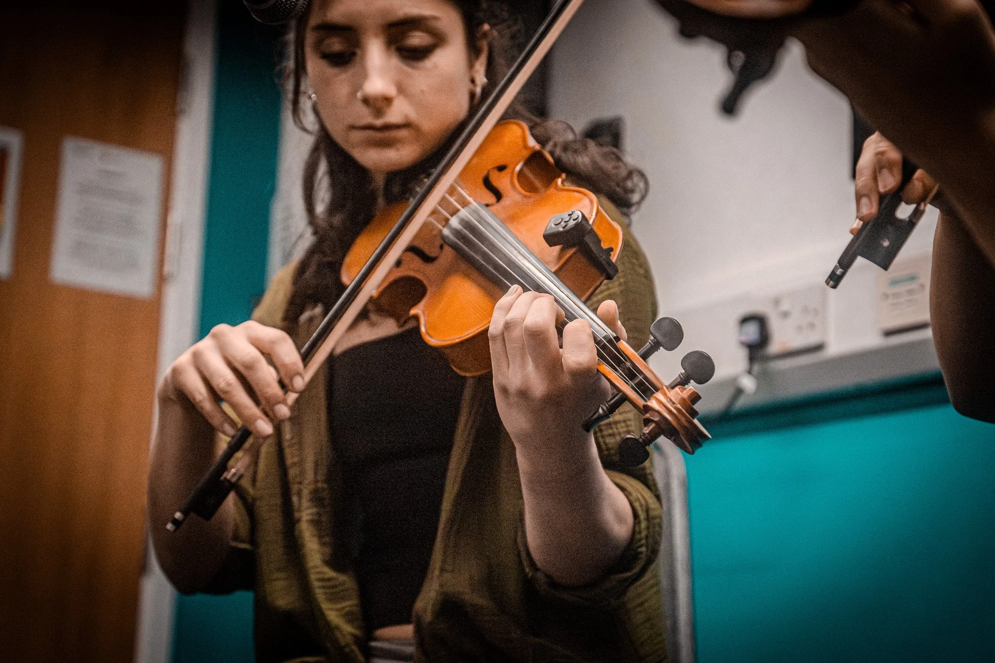 A young woman playing a violin while reading sheet music in what appears to be a music practice room.