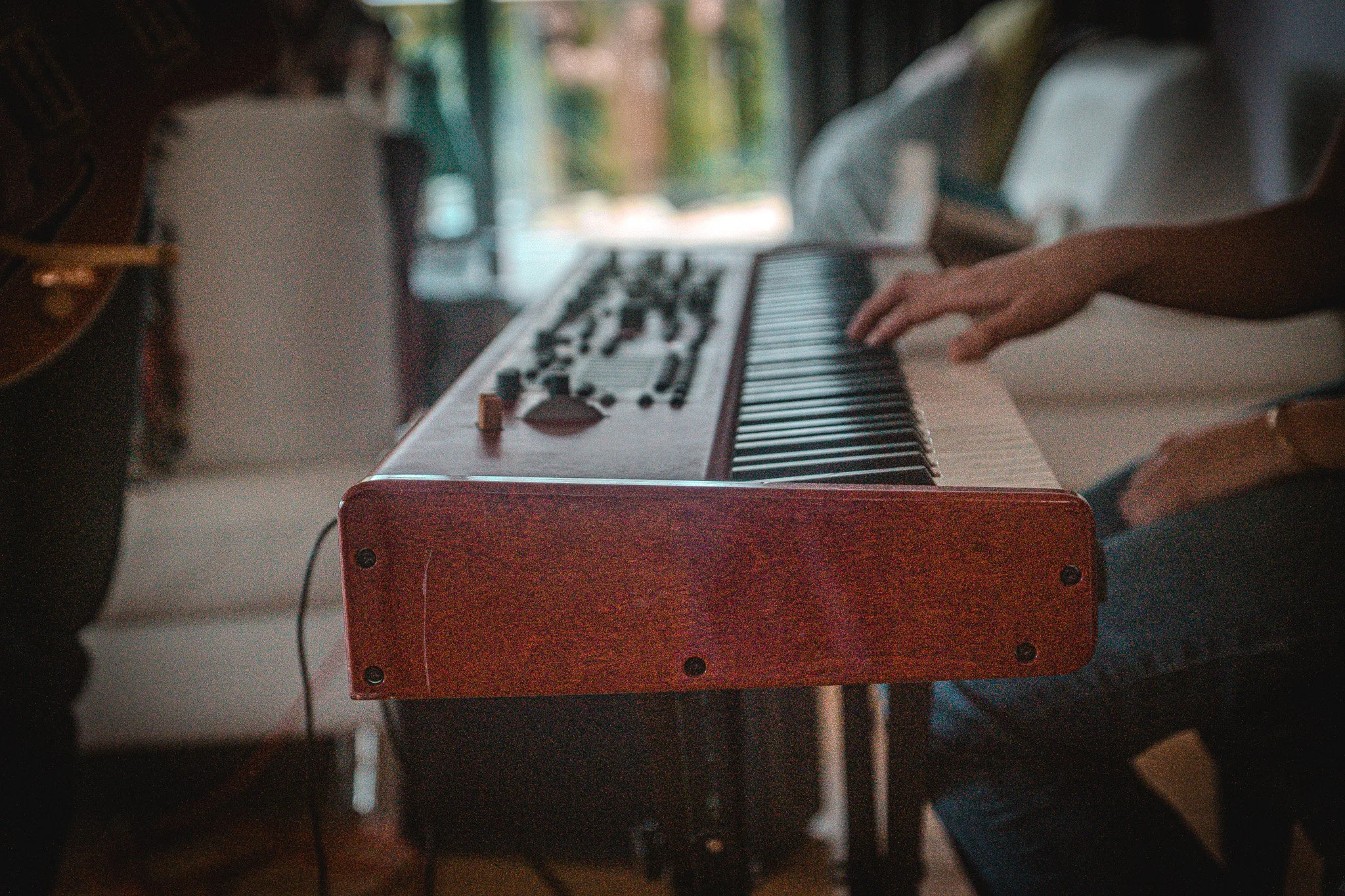 Person playing a keyboard with a red wood finish, in what appears to be a cozy indoor setting.