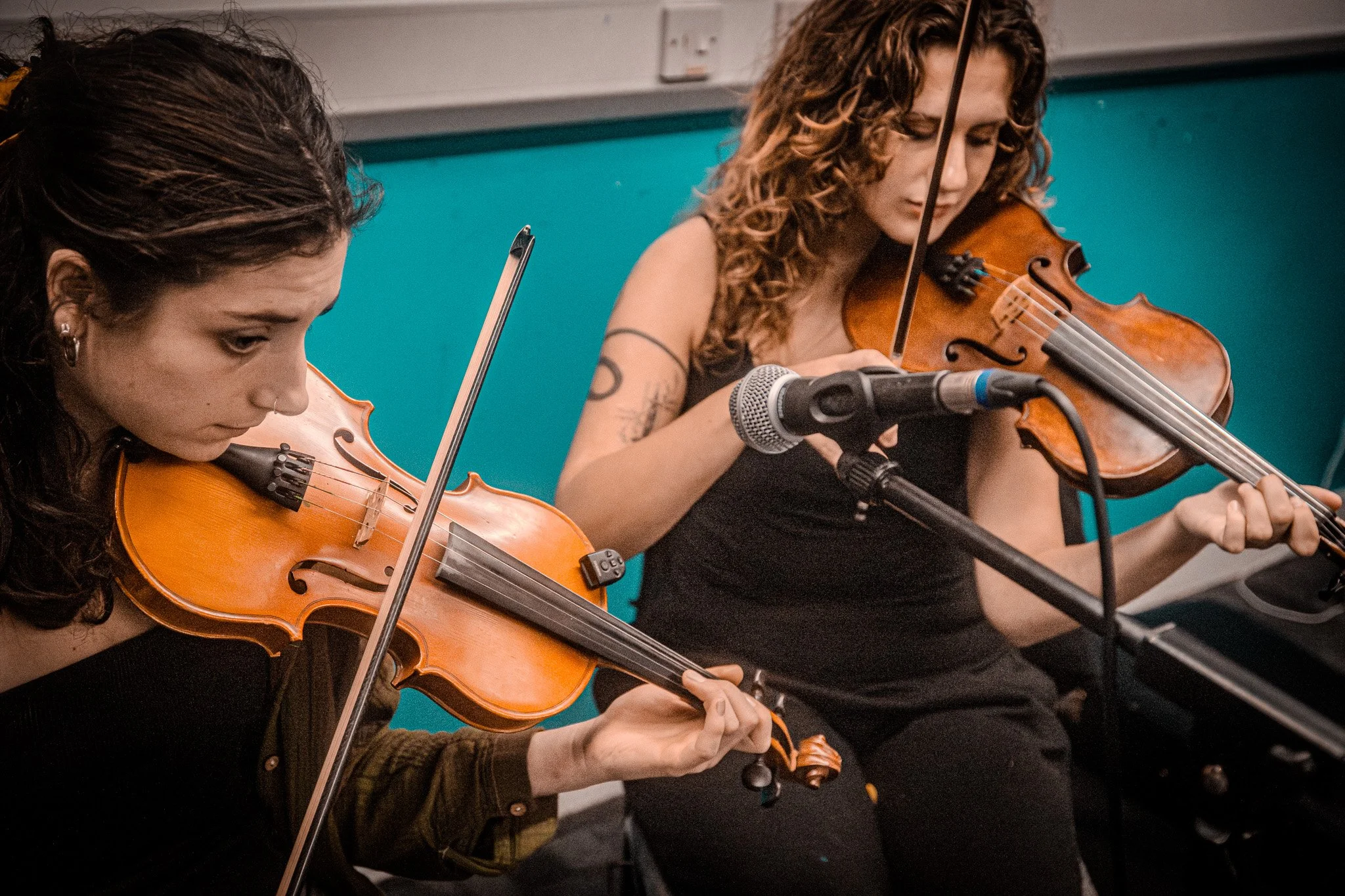 Two women playing violins in a music rehearsal or performance setting.