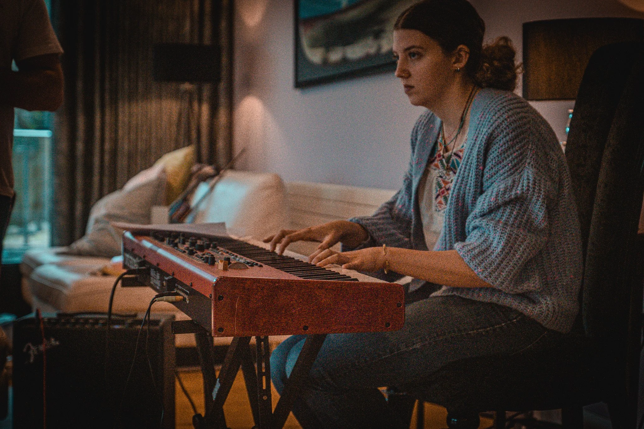 A woman playing a keyboard in a cozy, dimly lit room with artwork on the wall.