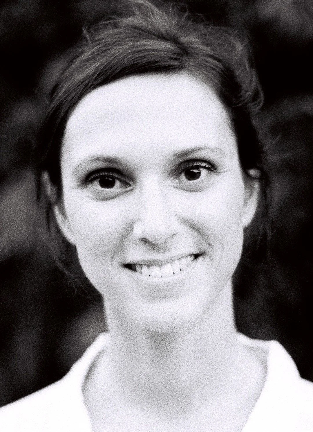 Black and white portrait of a smiling woman with short hair, wearing a white top.
