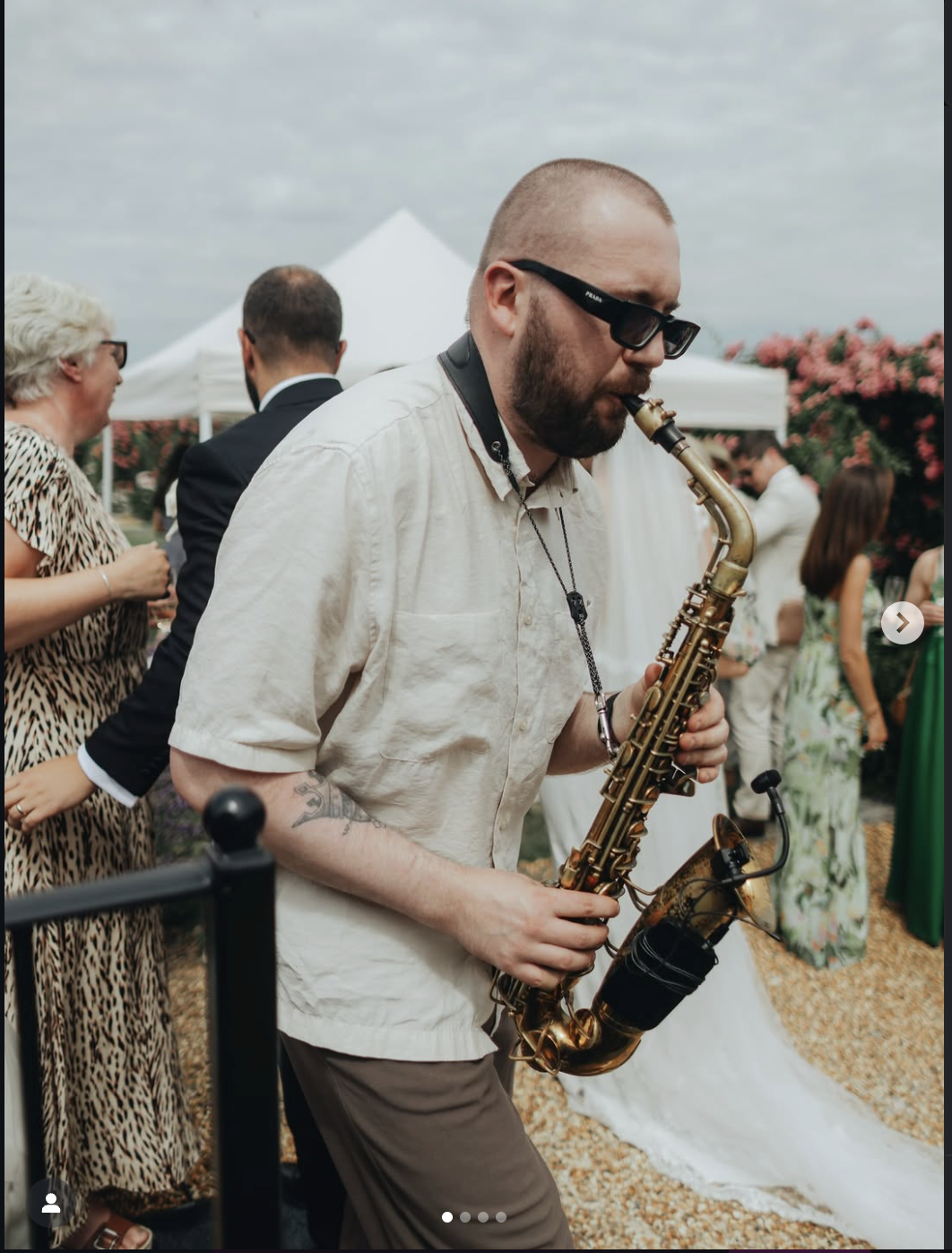 Musician playing saxophone at outdoor event with people in the background.