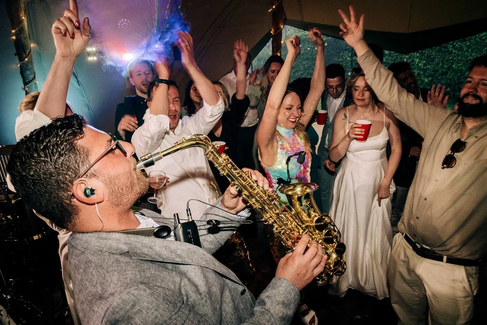 People dancing and enjoying live jazz music at a celebration or party, with a musician playing the saxophone and smiling guests with drinks