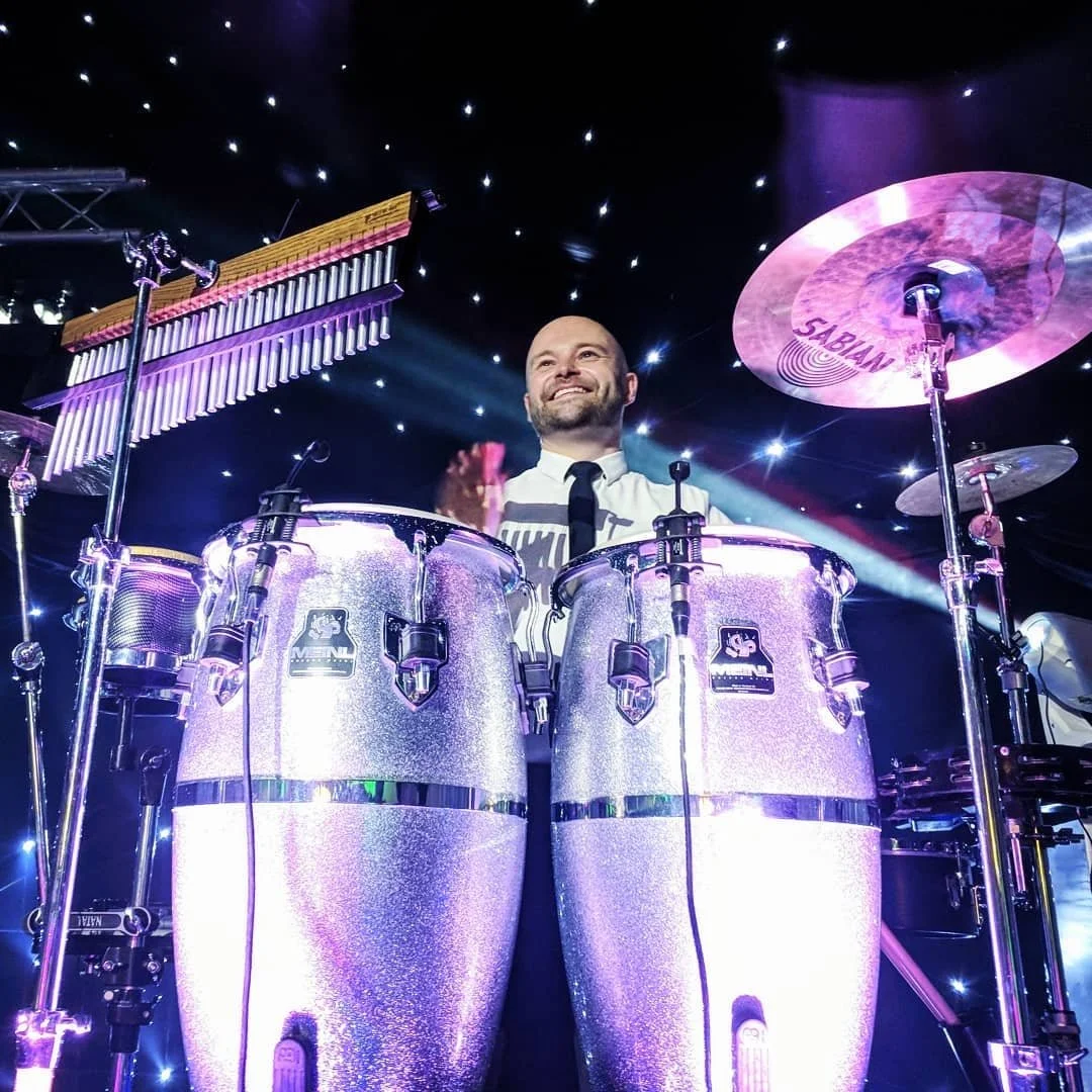 A drummer playing a drum set during a concert with a starry background and stage lighting.