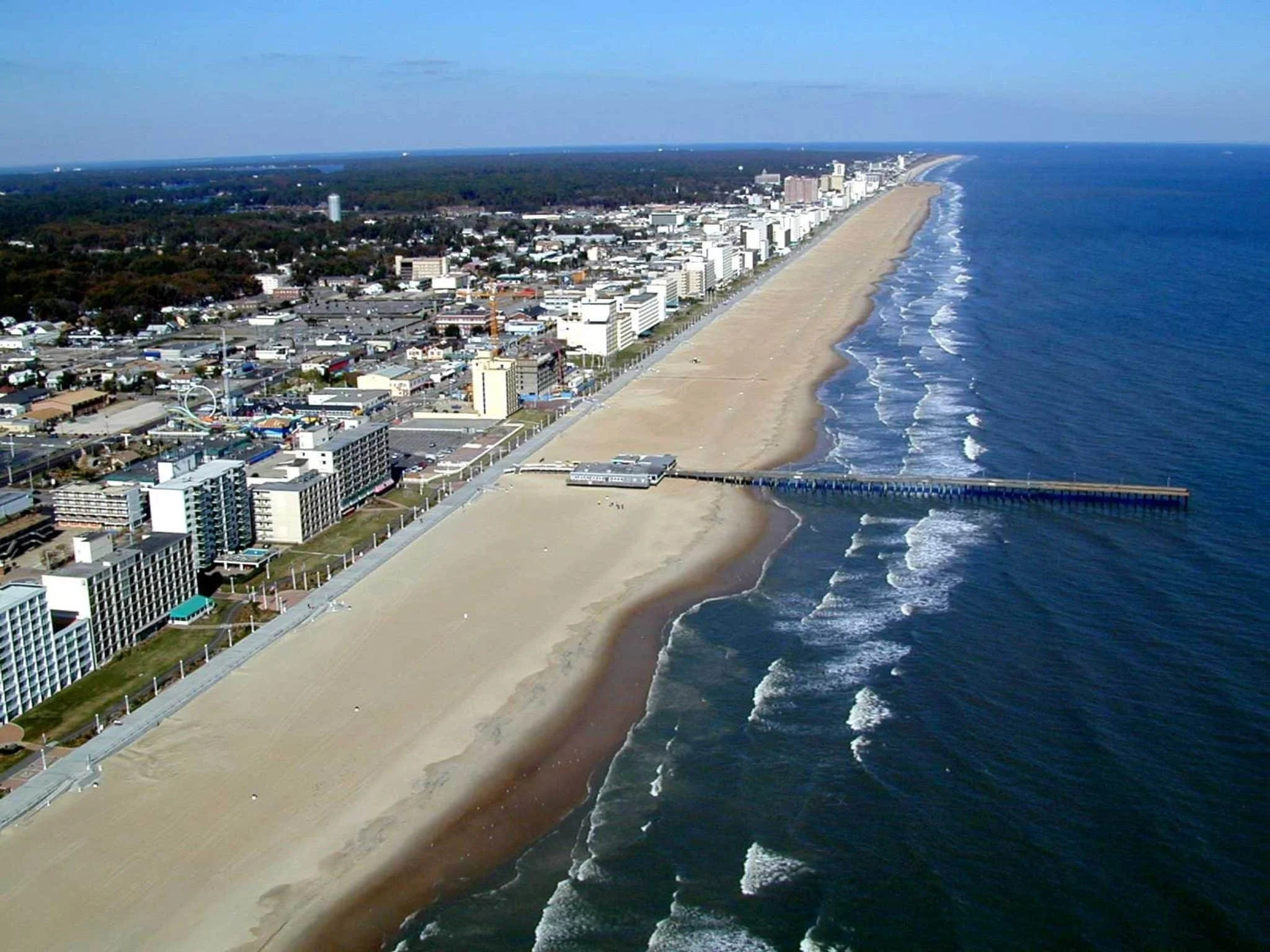 Aerial view of a beachside city with high-rise buildings, a long sandy beach, and a pier extending into the ocean.