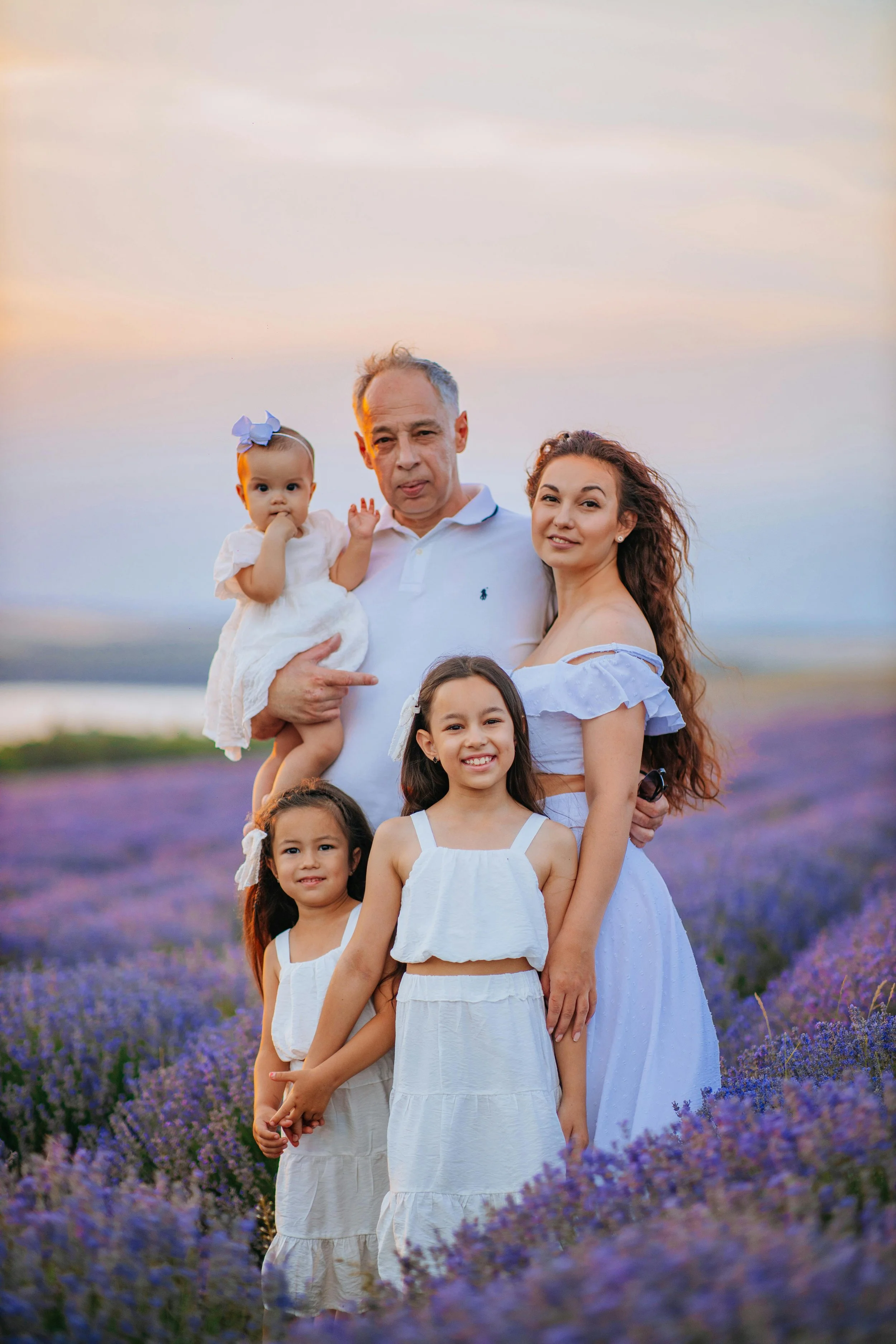 Family of six posing in a lavender field at sunset, with purple flowers and a blue sky in the background. Family Photography