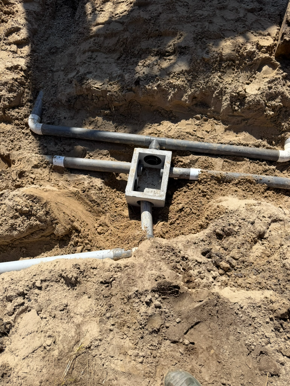 Underground plumbing pipes and fittings in a dirt excavation site for construction or repair.