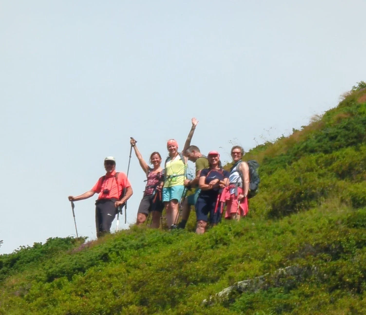 Eine Gruppe von Wanderern steht auf einem grünen Hügel und freut sich, während sie in der Natur unterwegs sind.
