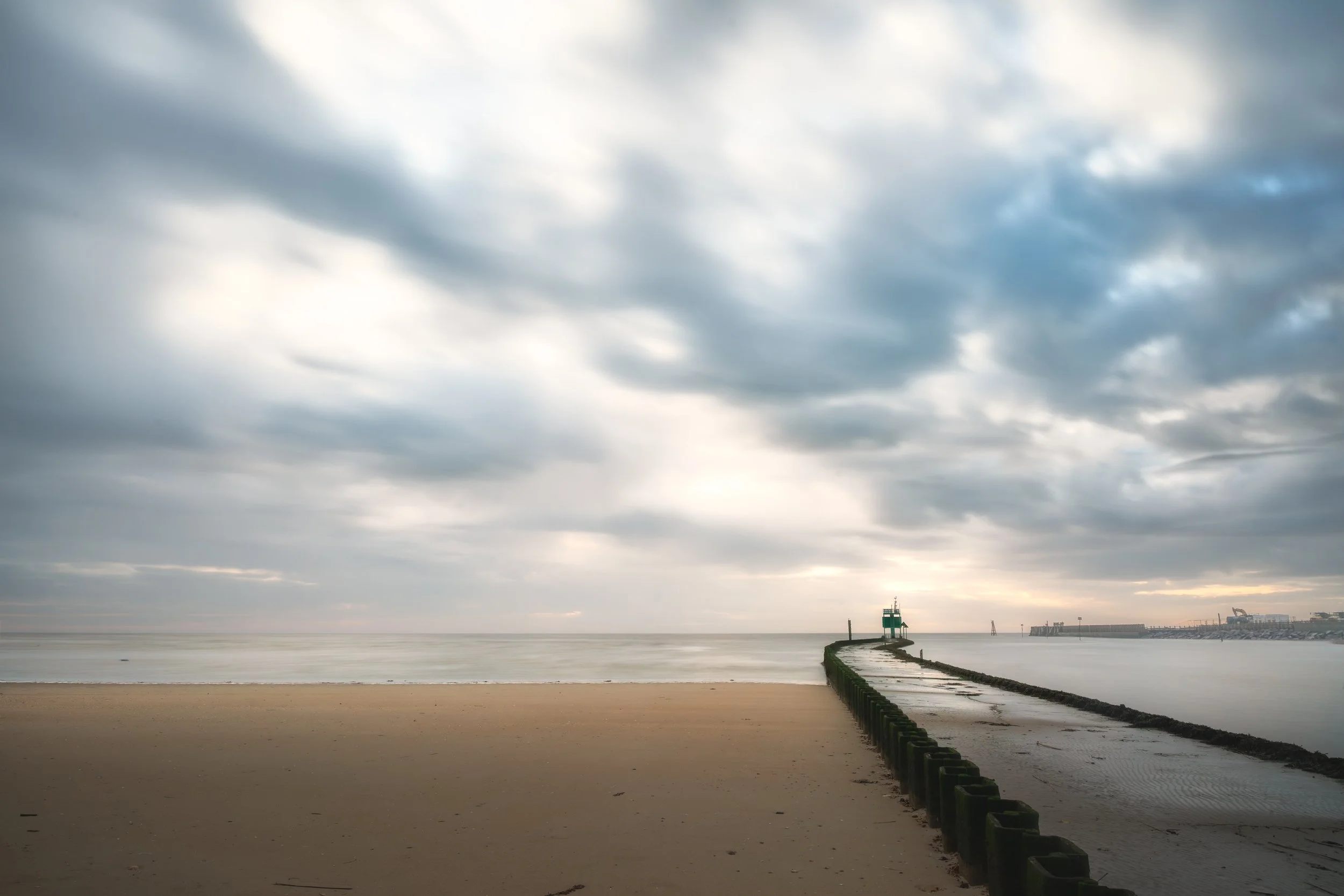 Empty beach with a jetty leading into the ocean, under cloudy sky.