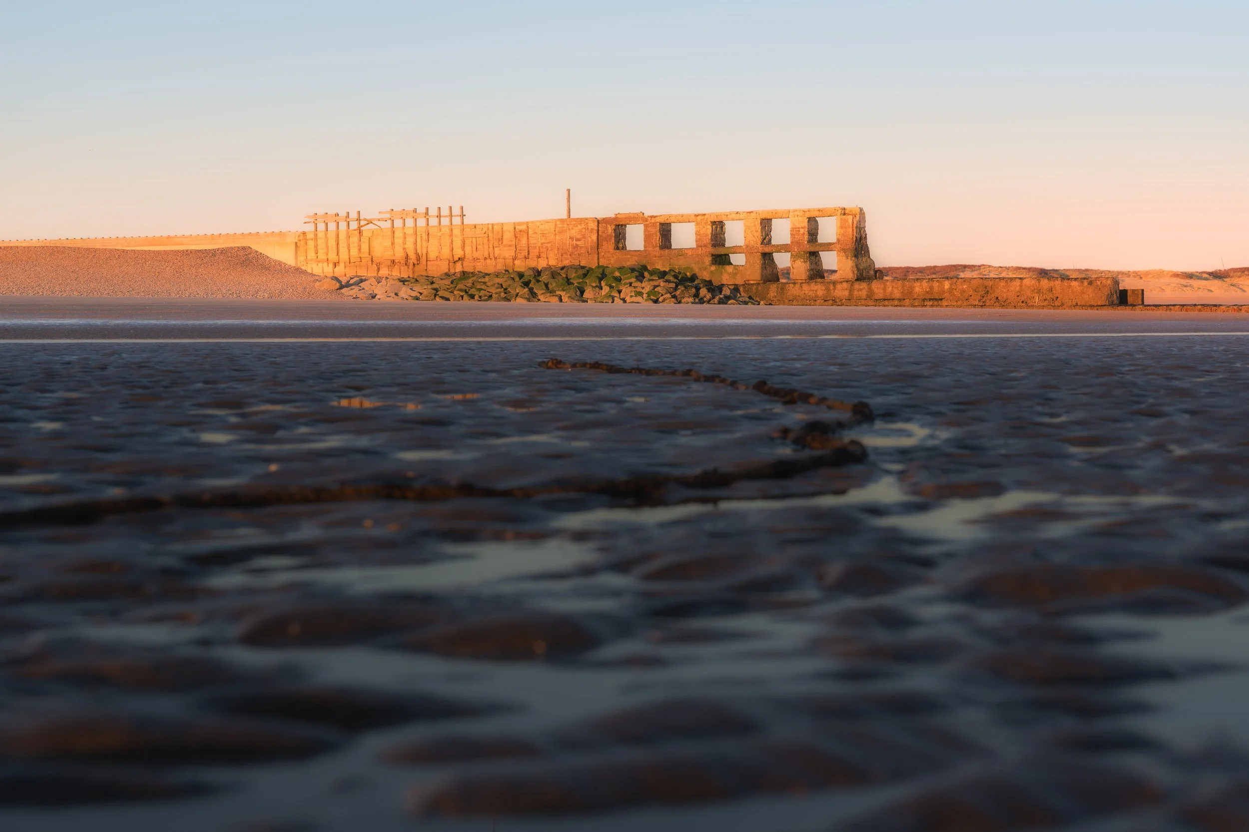 Photo of a beach with an old concrete structure and rocks, taken at sunset or sunrise.