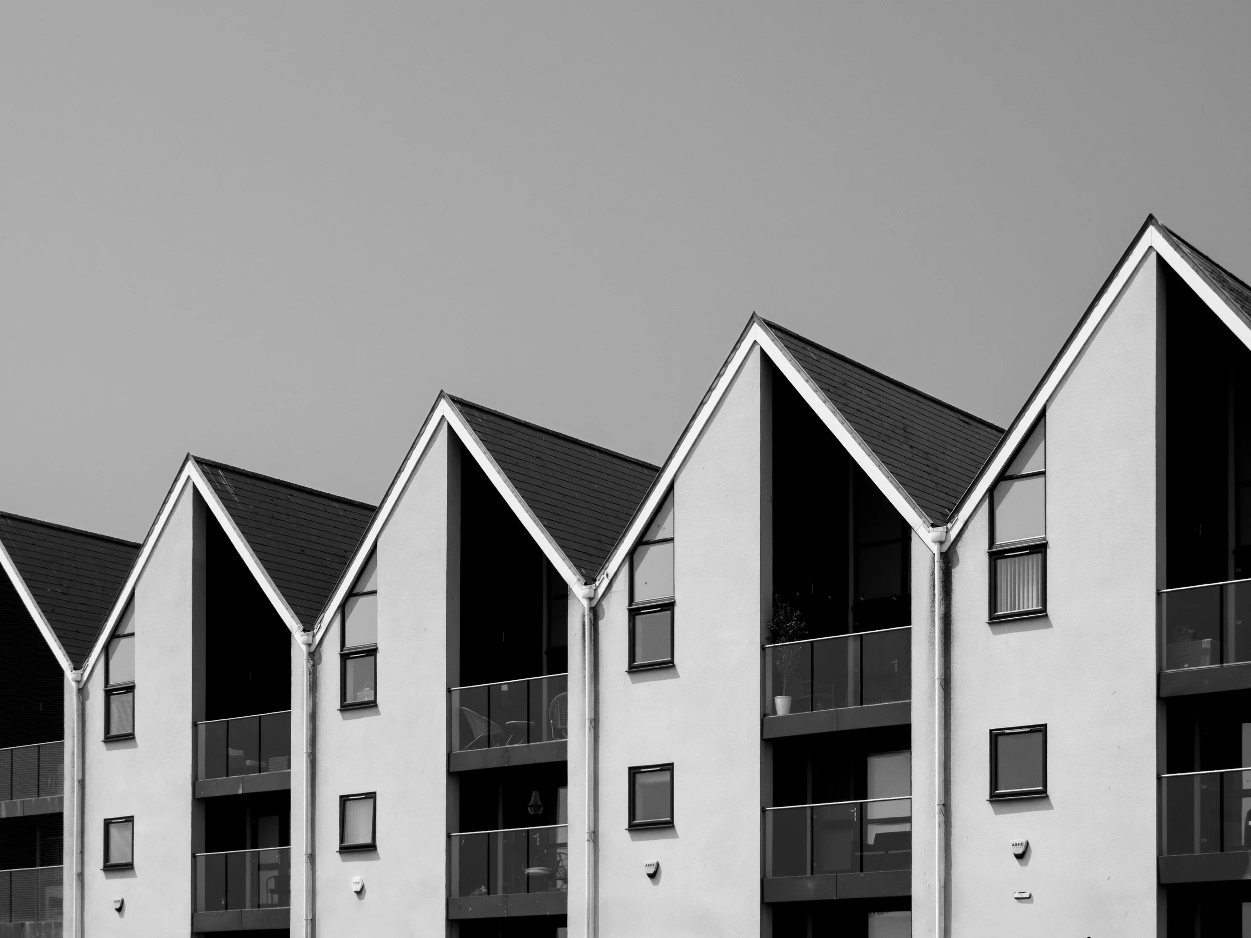 Black and white photo of modern apartment building with triangular rooflines and balconies.