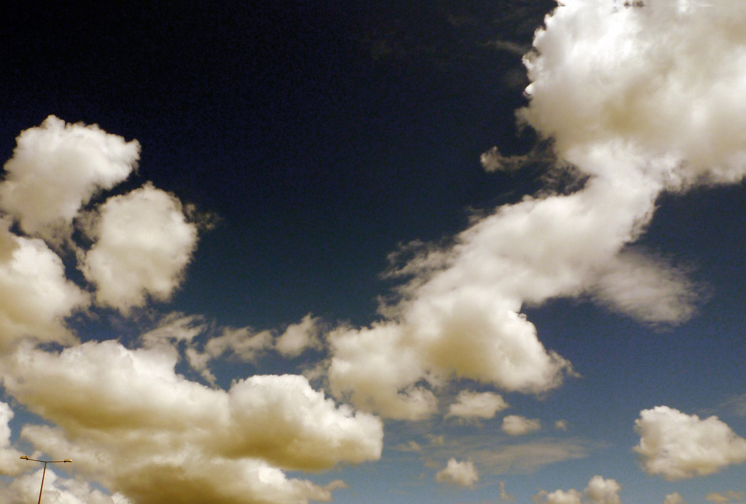 Cloud-filled sky with large white clouds and a small portion of a streetlight at the bottom left.
