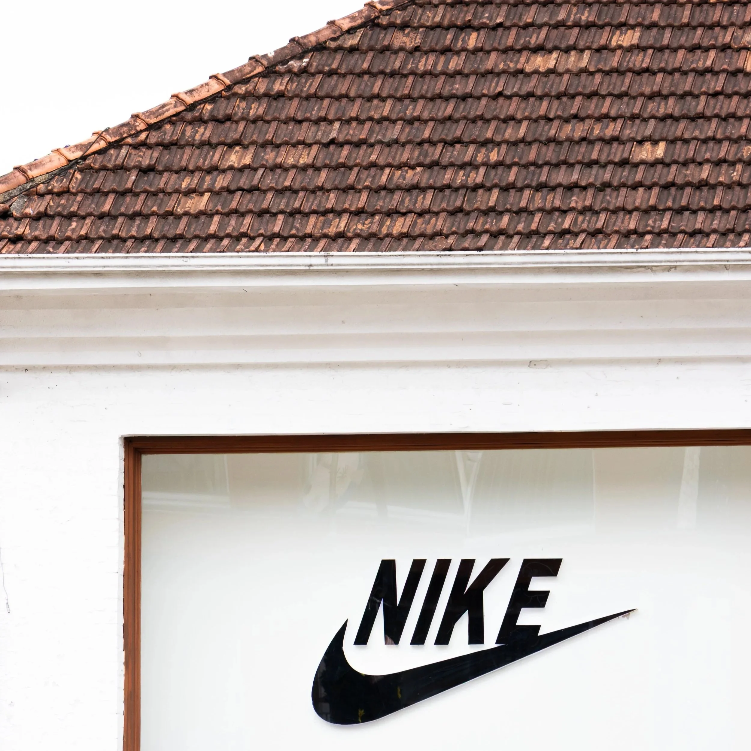 Letreiro com o logo da Nike na fachada de uma loja, com a parte superior de um telhado de telhas de cerâmica visível.