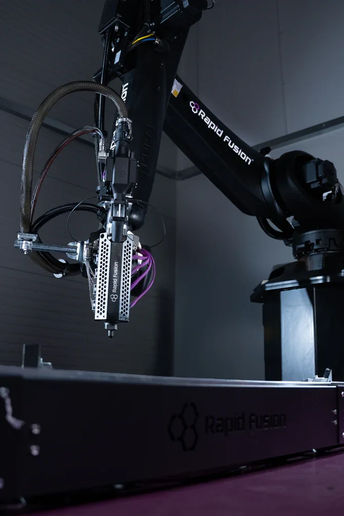 Close-up of a robotic arm with the label 'Rapid Fusion', positioned over a tray or platform, in a modern laboratory or manufacturing setting.