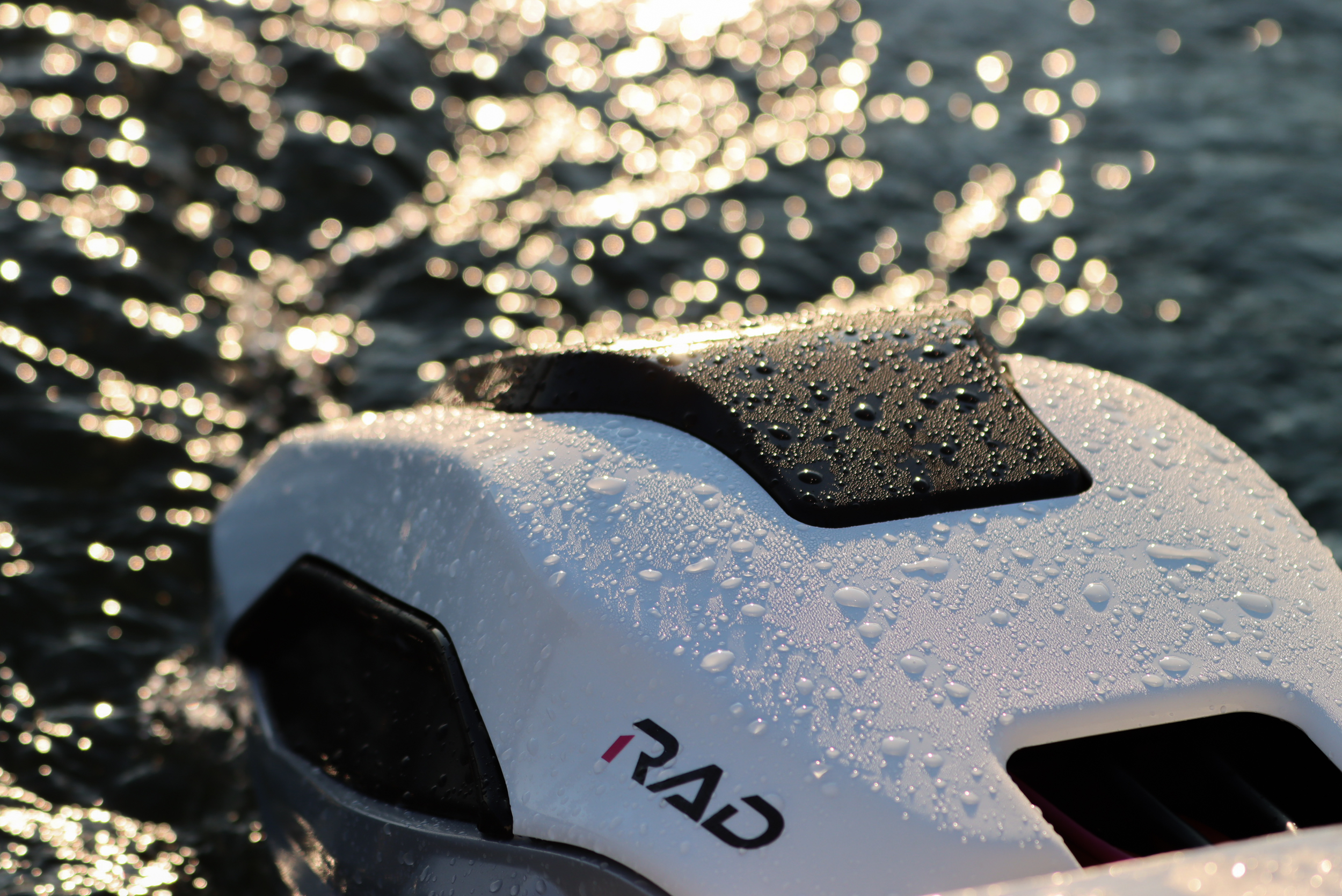 Close-up of a white object with water droplets on it, partially submerged in water with sunlight reflecting off the surface, creating a bokeh effect in the background.