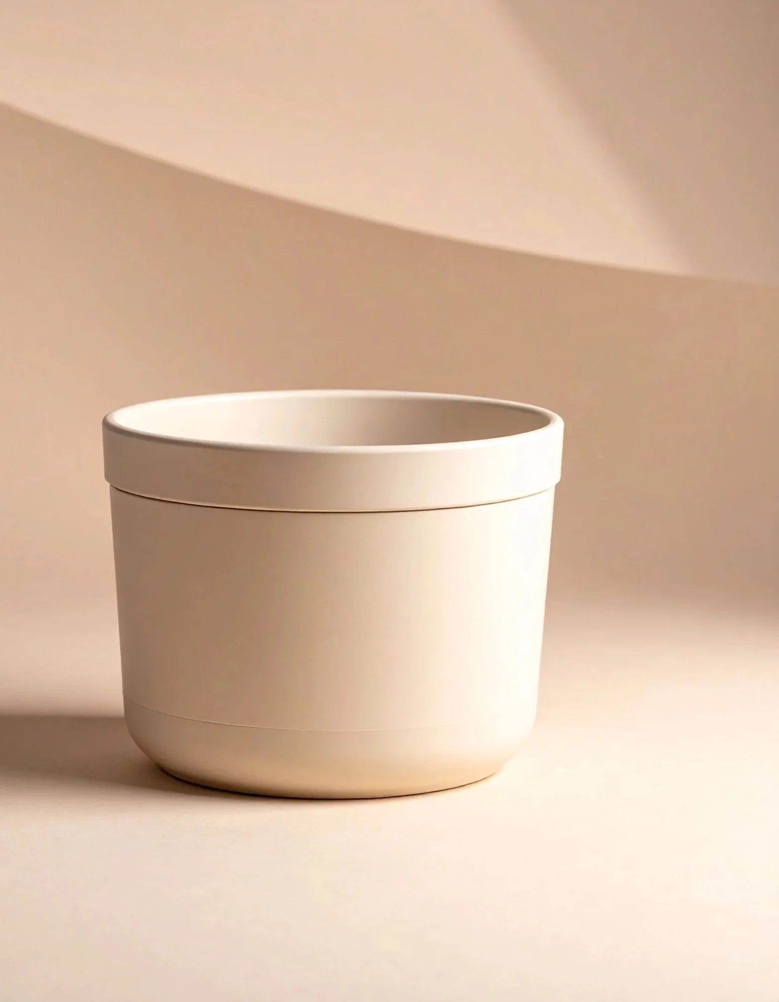 A minimalistic, matte white container with a closed lid on a light cream surface, with soft shadows and beige background.